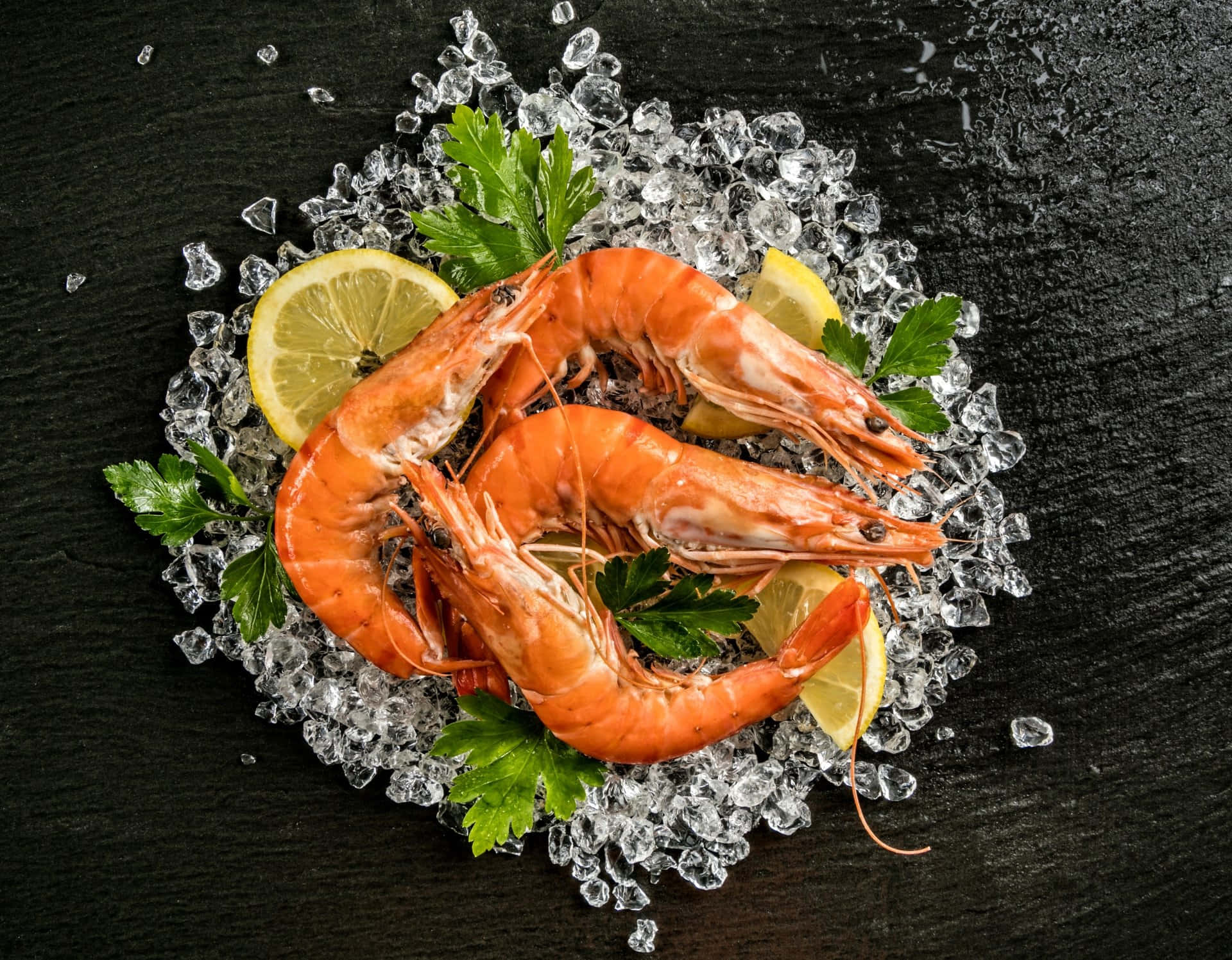 Seafood 桌布 壁紙 — 三隻鮮橙色熟蝦放在碎冰上，搭配檸檬片和歐芹，置於深色石板表面。