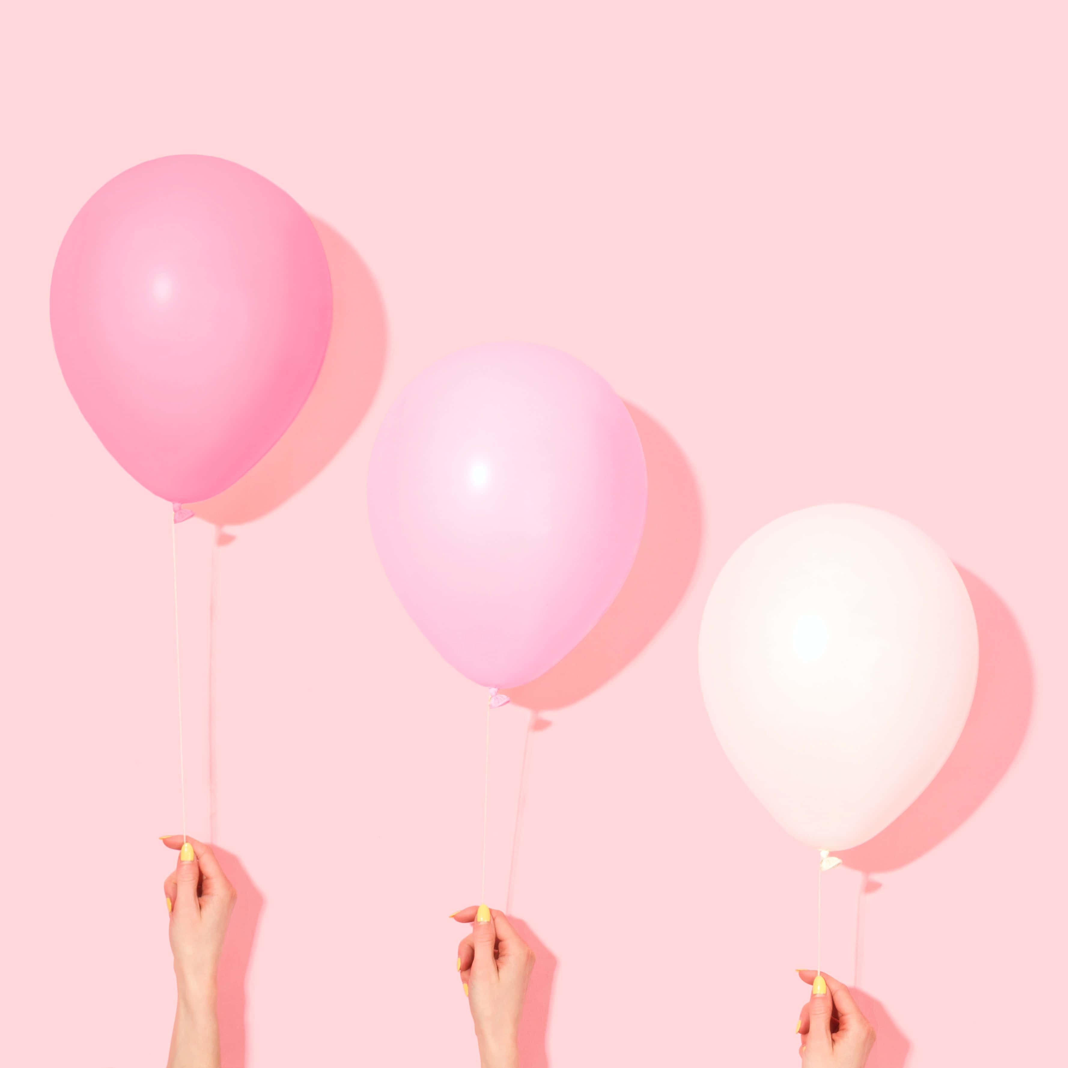 Balloons 桌布 壁紙 — 三隻黃色指甲的手拿著粉紅色和白色的氣球，背景為純粉紅色。