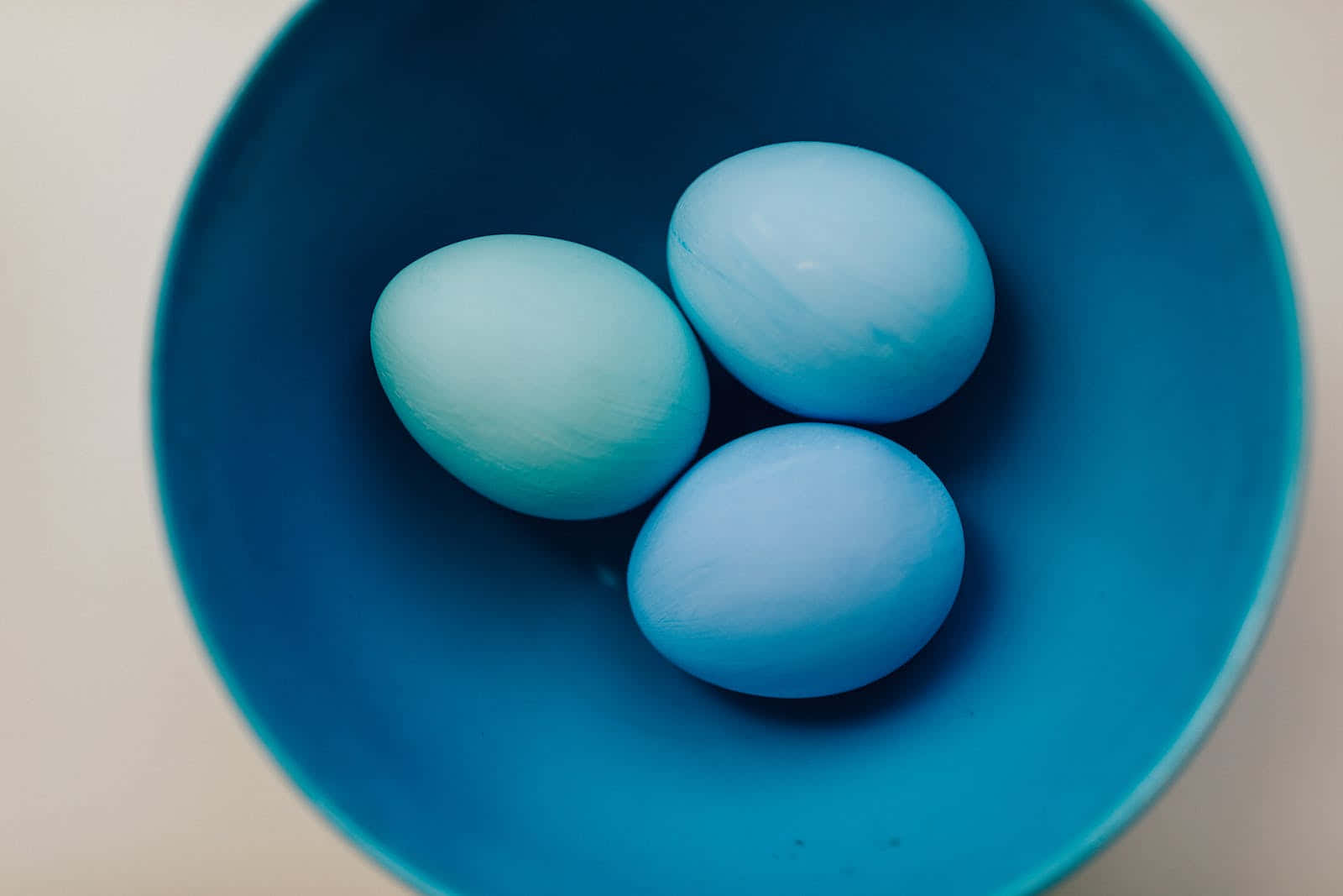 Pastel Easter 桌布 壁紙 — 三顆光滑的藍色雞蛋放在一個相配的藍色碗中，背景柔和中性。