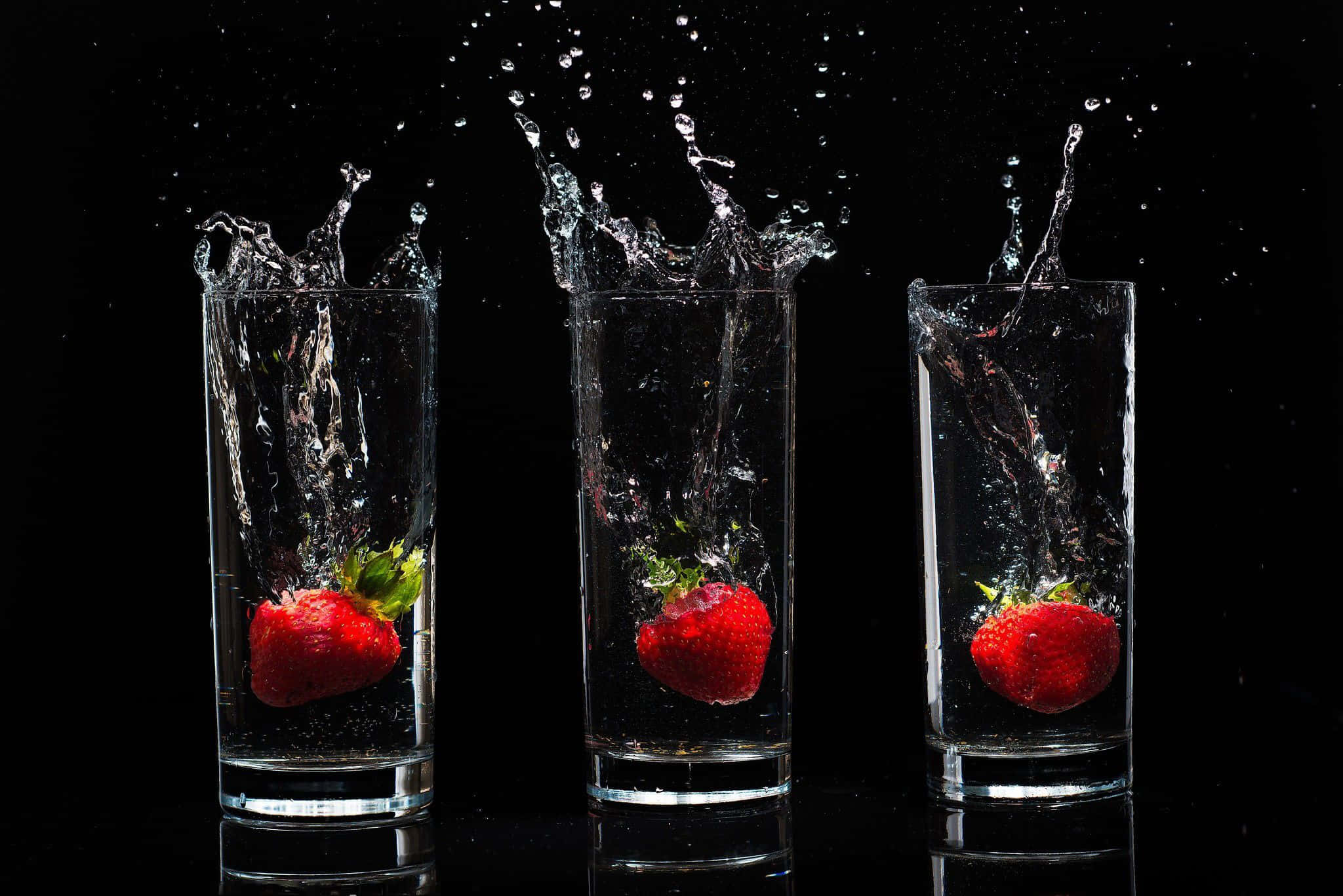 Glass Of Water 桌布 壁紙 — 三顆成熟的草莓掉入水中，在黑色背景上產生戲劇性的水花。