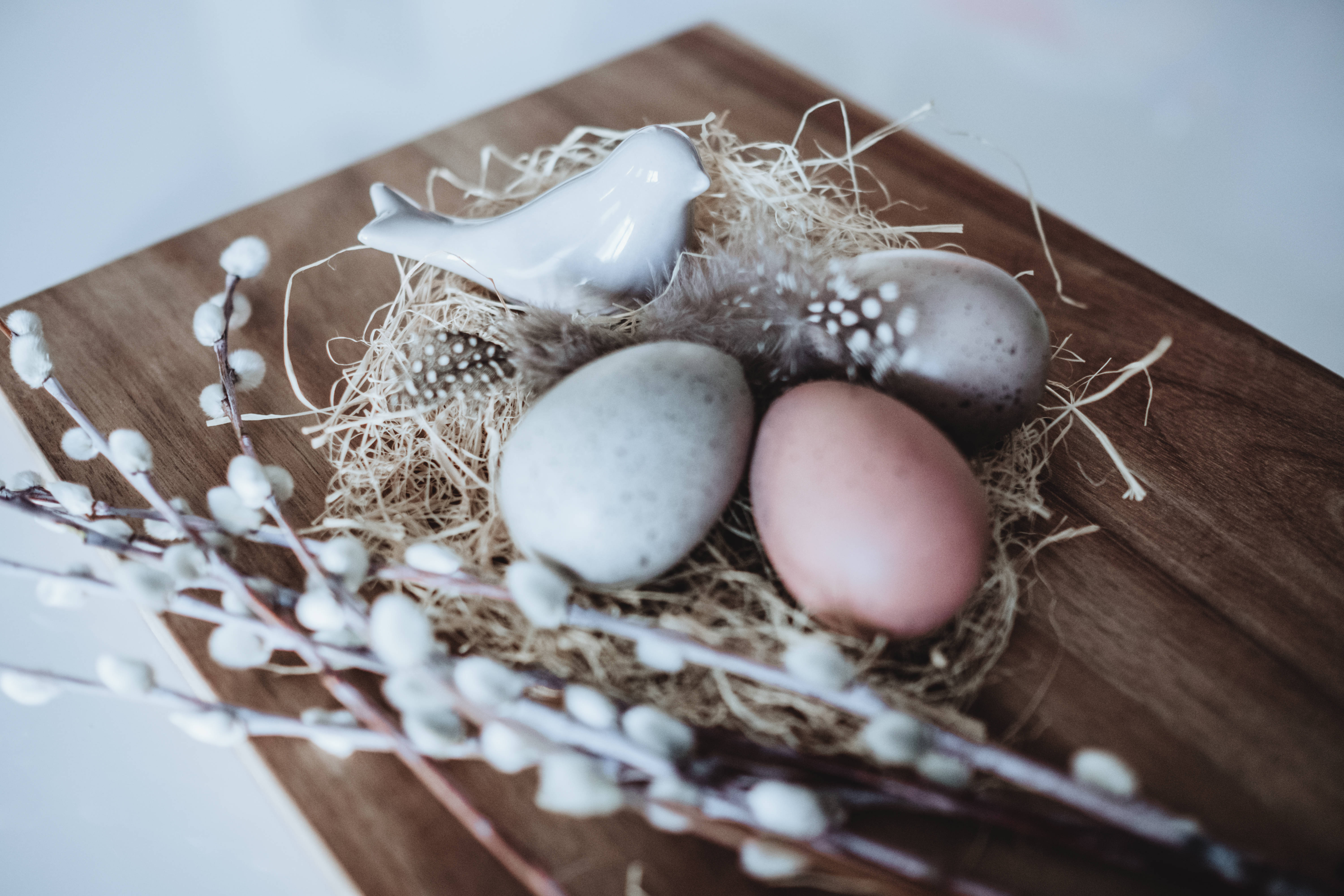 Happy Easter 桌布 壁紙 — 三顆有斑點的蛋和一隻陶瓷鳥放在柳枝旁邊的木板上稻草中。