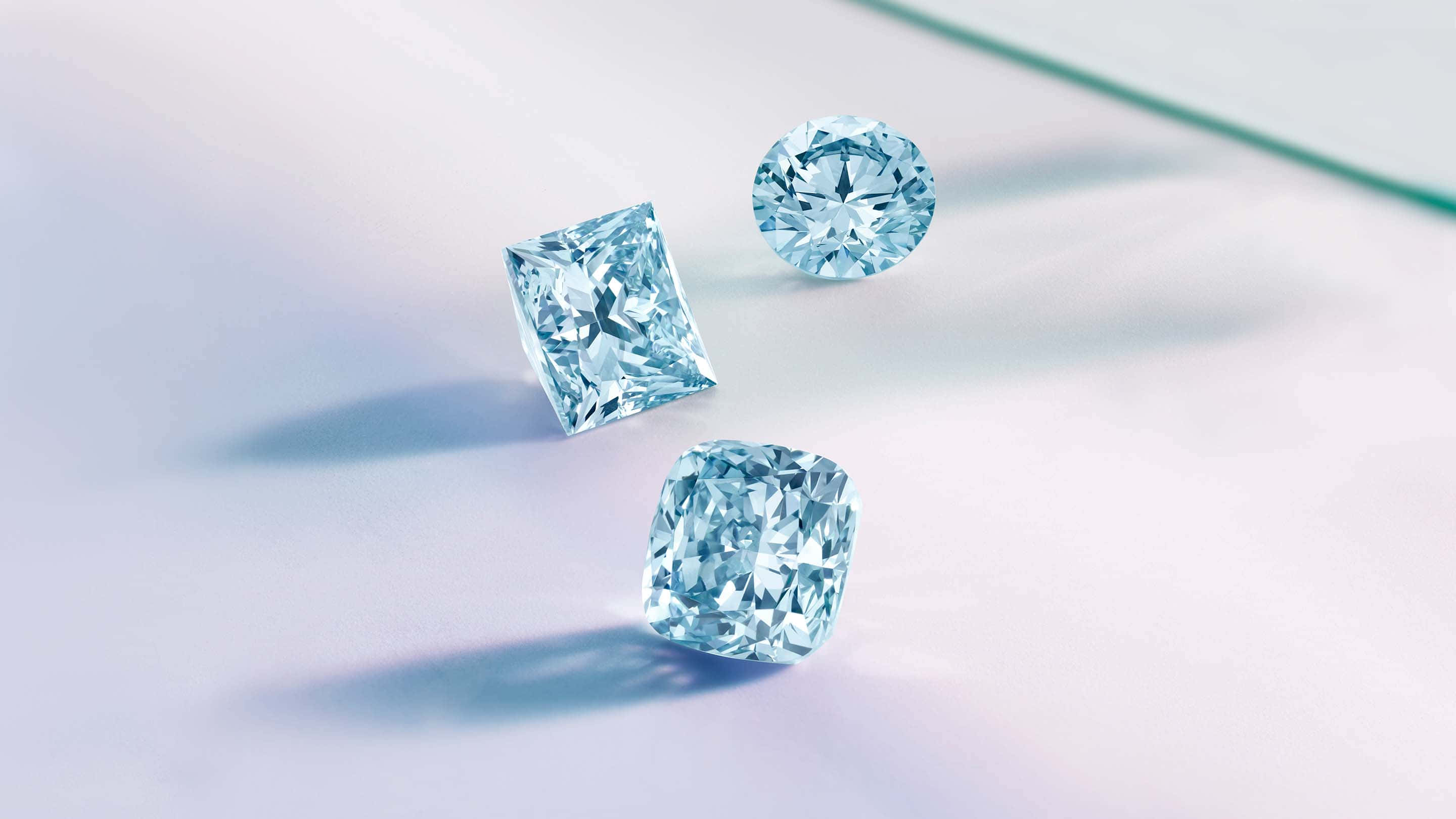 Blue Diamonds 桌布 壁紙 — 三顆淺藍色鑽石，切割精準，在柔和光線下於淺色表面上閃爍。