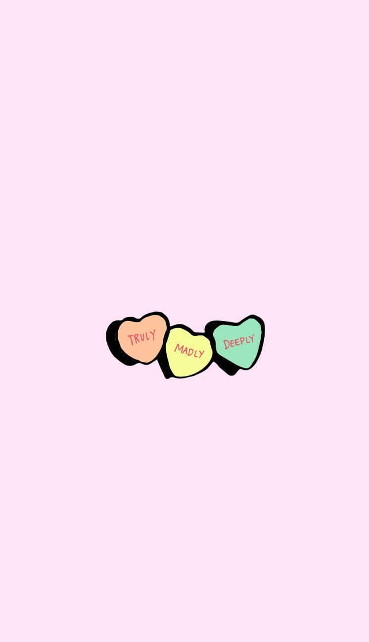 Cute Valentines 桌布 壁紙 — 三顆粉彩色心形糖果，上面寫著 truly madly deeply，放在柔和的粉紅色背景上。