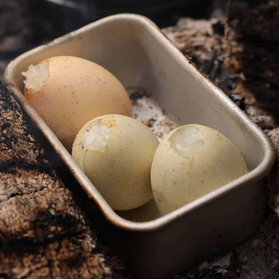 Eggshell 桌布 壁紙 — 三顆蛋殼破裂的雞蛋放在一個金屬托盤中，托盤置於悶燒的灰燼和燒焦的木頭之間。