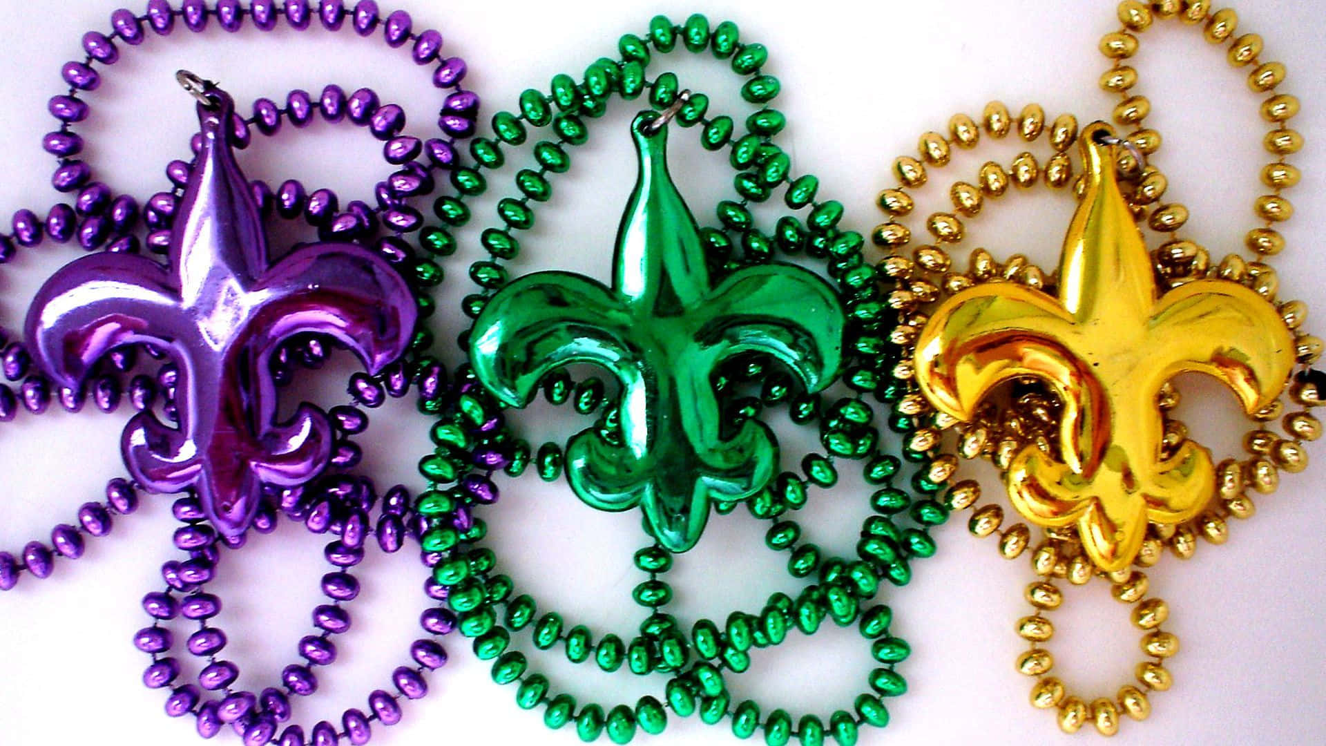 Mardi Gras 桌布 壁紙 — 三顆閃亮的狂歡節珠子，分別為紫色、綠色和金色，每顆頂部都有一個相配的百合花飾物。