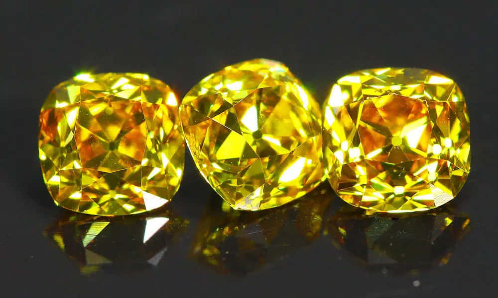 Yellow Diamond 桌布 壁紙 — 三顆閃耀的黃色寶石，帶有精細切割面，在深色反光表面上閃爍光芒。
