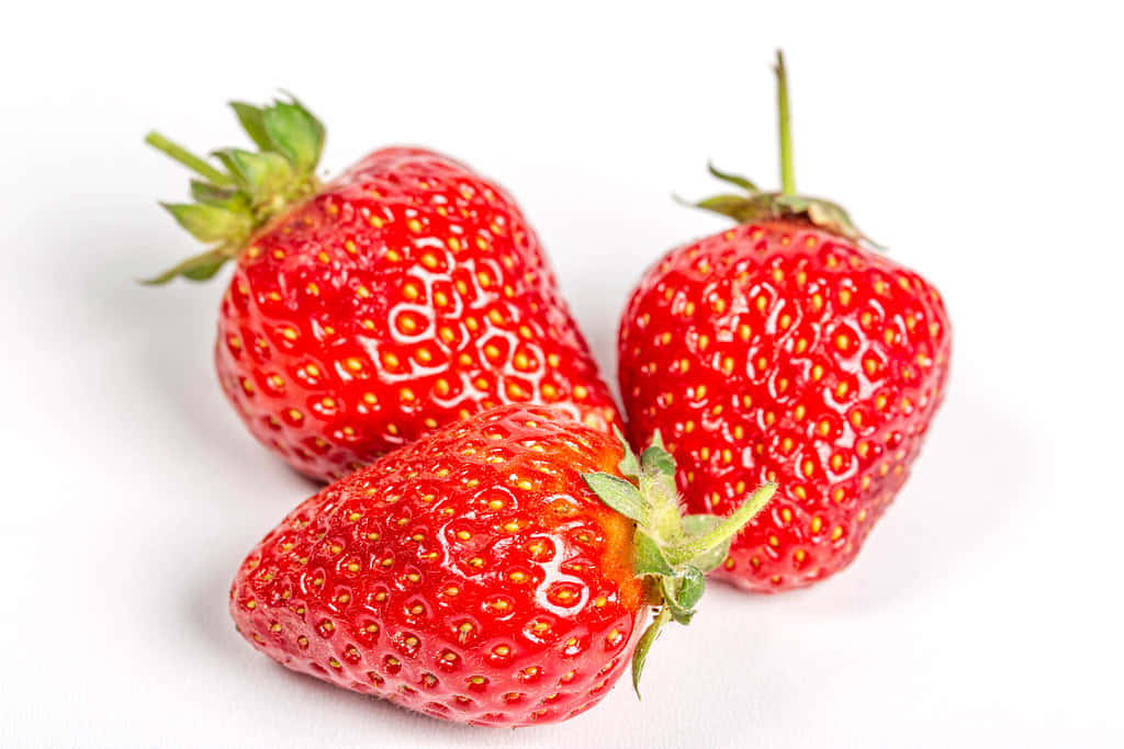 Strawberries 桌布 壁紙 — 三顆飽滿成熟的草莓，頂部帶有綠色葉子，放在潔白的表面上，展現多汁的質感。