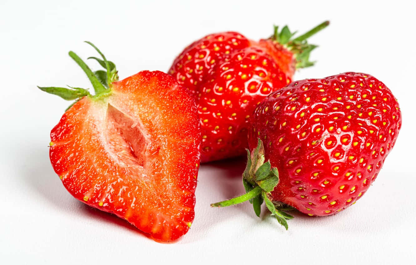 Strawberries 桌布 壁紙 — 三顆鮮紅草莓，其中一顆切半，露出多汁的內部，襯以潔白背景。