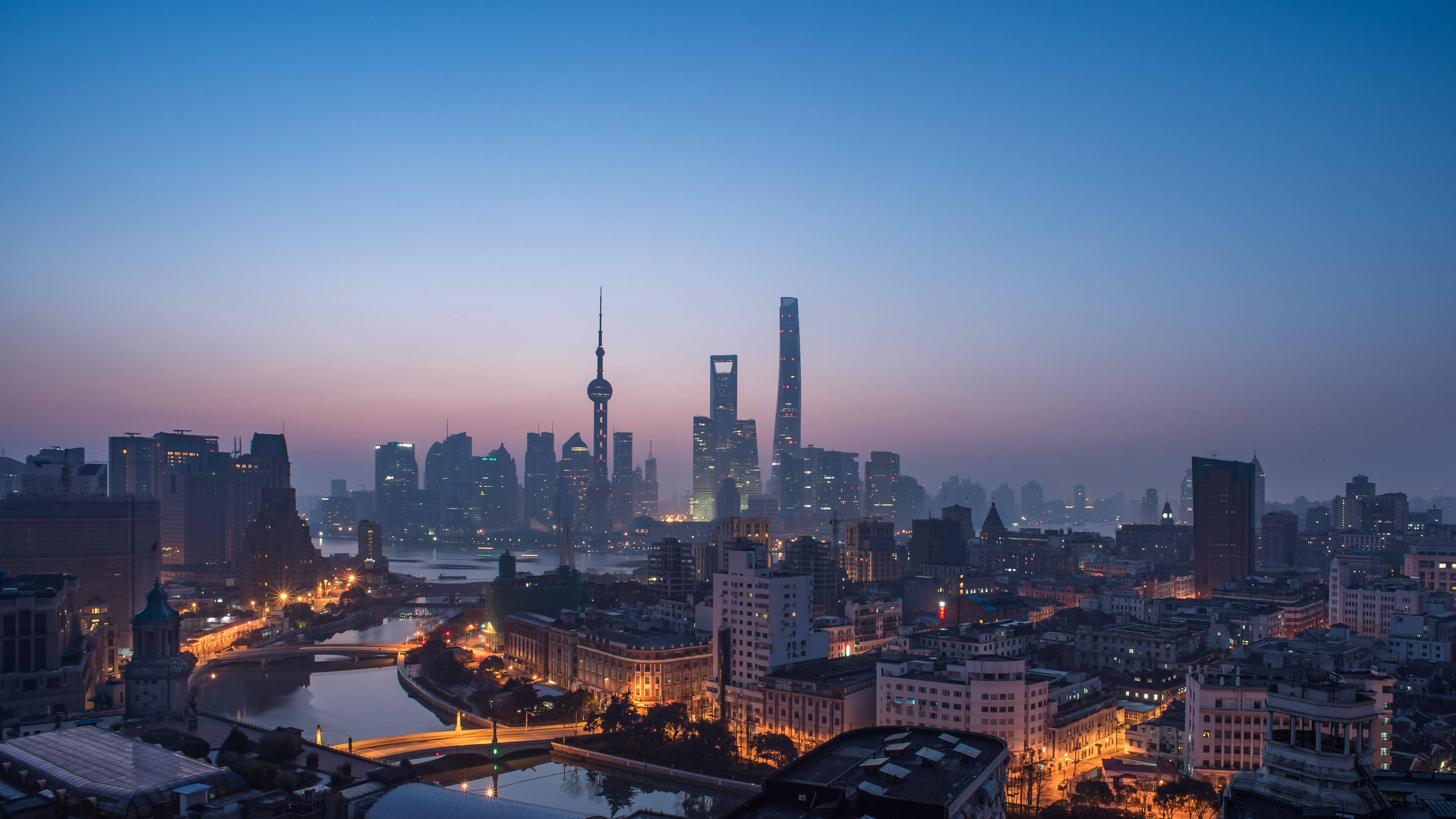 Asia 桌布 壁紙 — 上海天際線的黃昏全景，高樓大廈燈火通明，河流蜿蜒穿過城市。