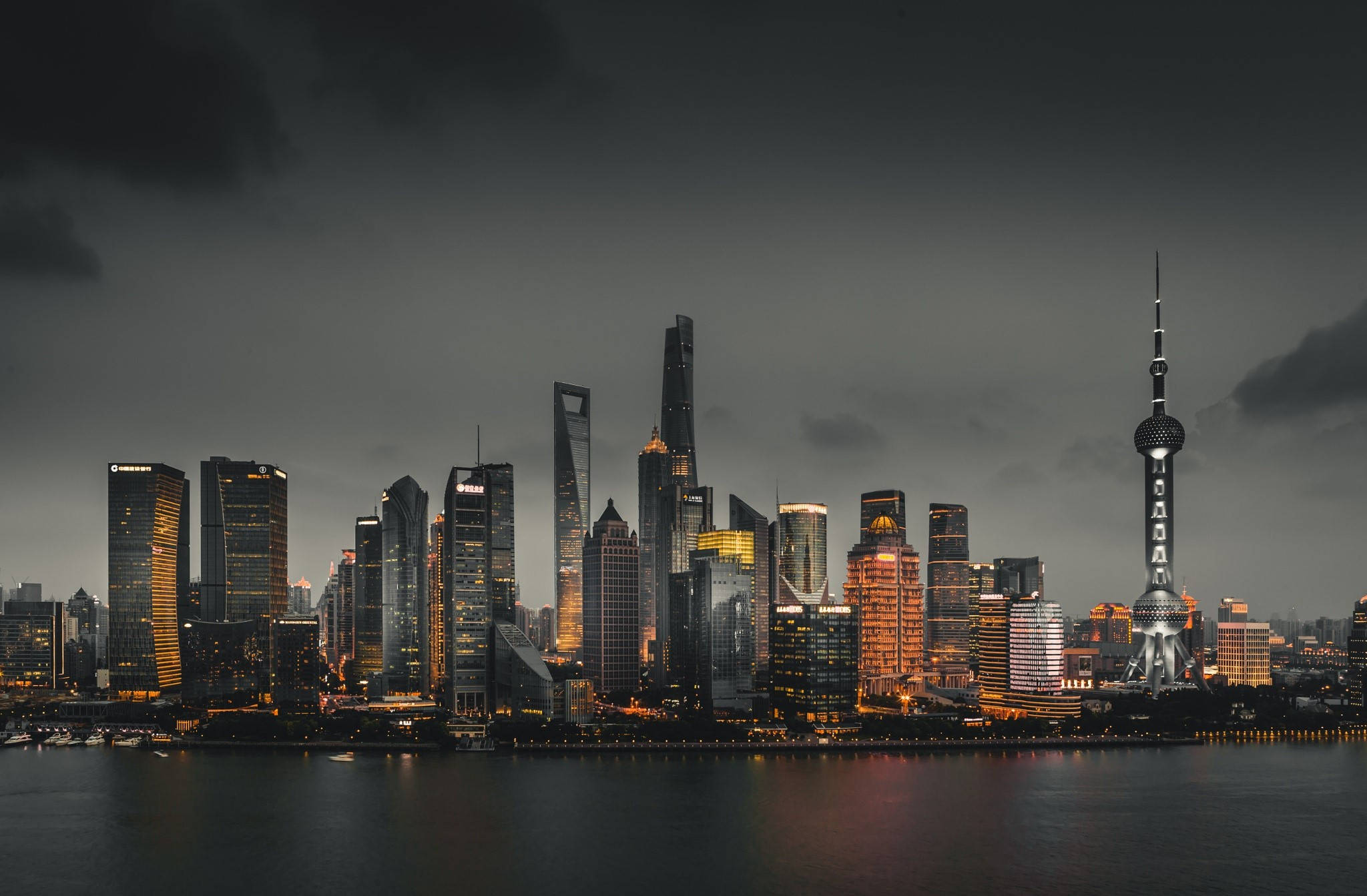 Asia 桌布 壁紙 — 上海現代摩天大樓在暴風雲下，金色燈光倒映在黑暗水面上，形成戲劇性的黃昏天際線。