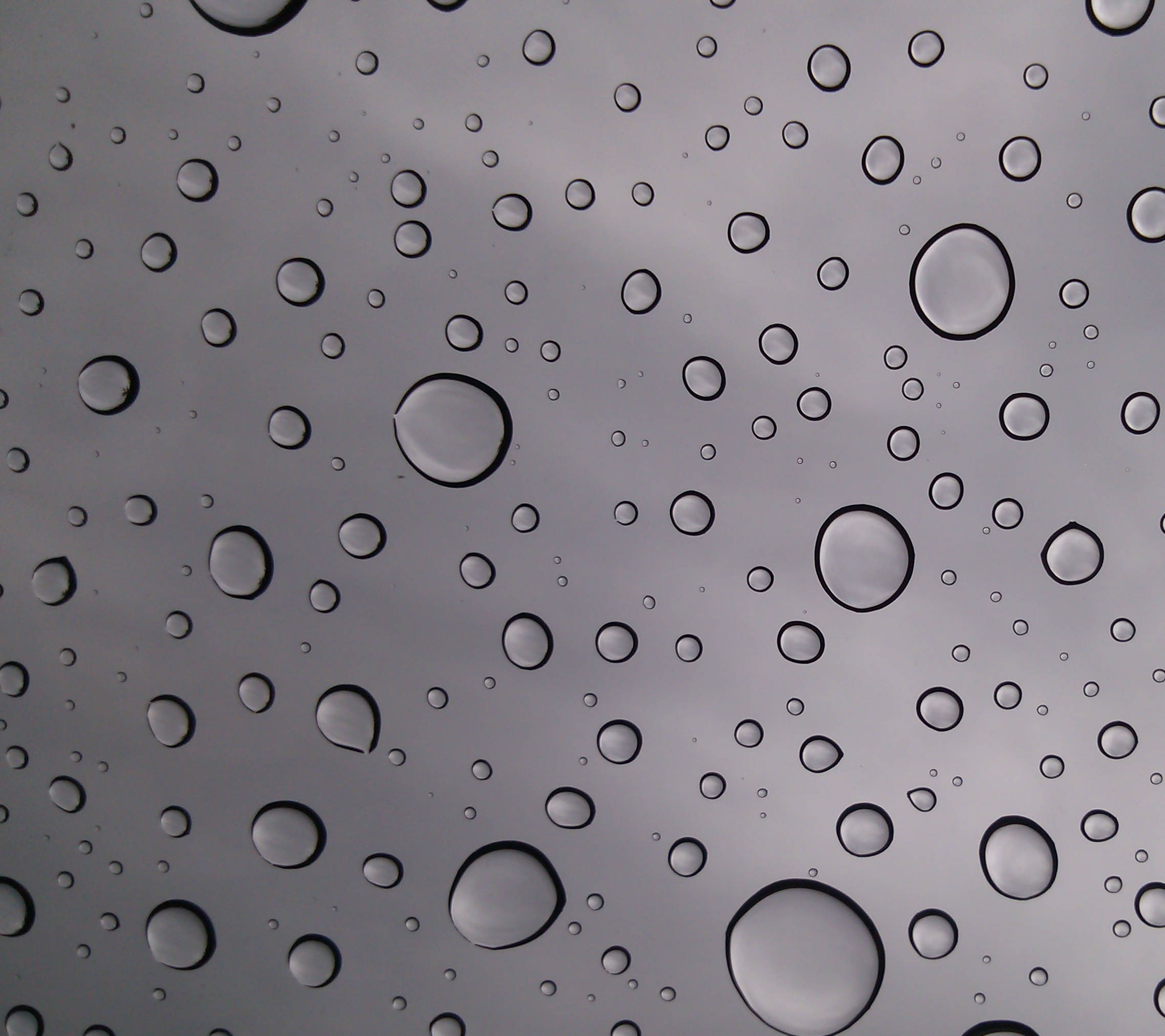 Basic 桌布 壁紙 — 不同大小的雨滴依附在玻璃表面，反射出暗淡的灰色天空。