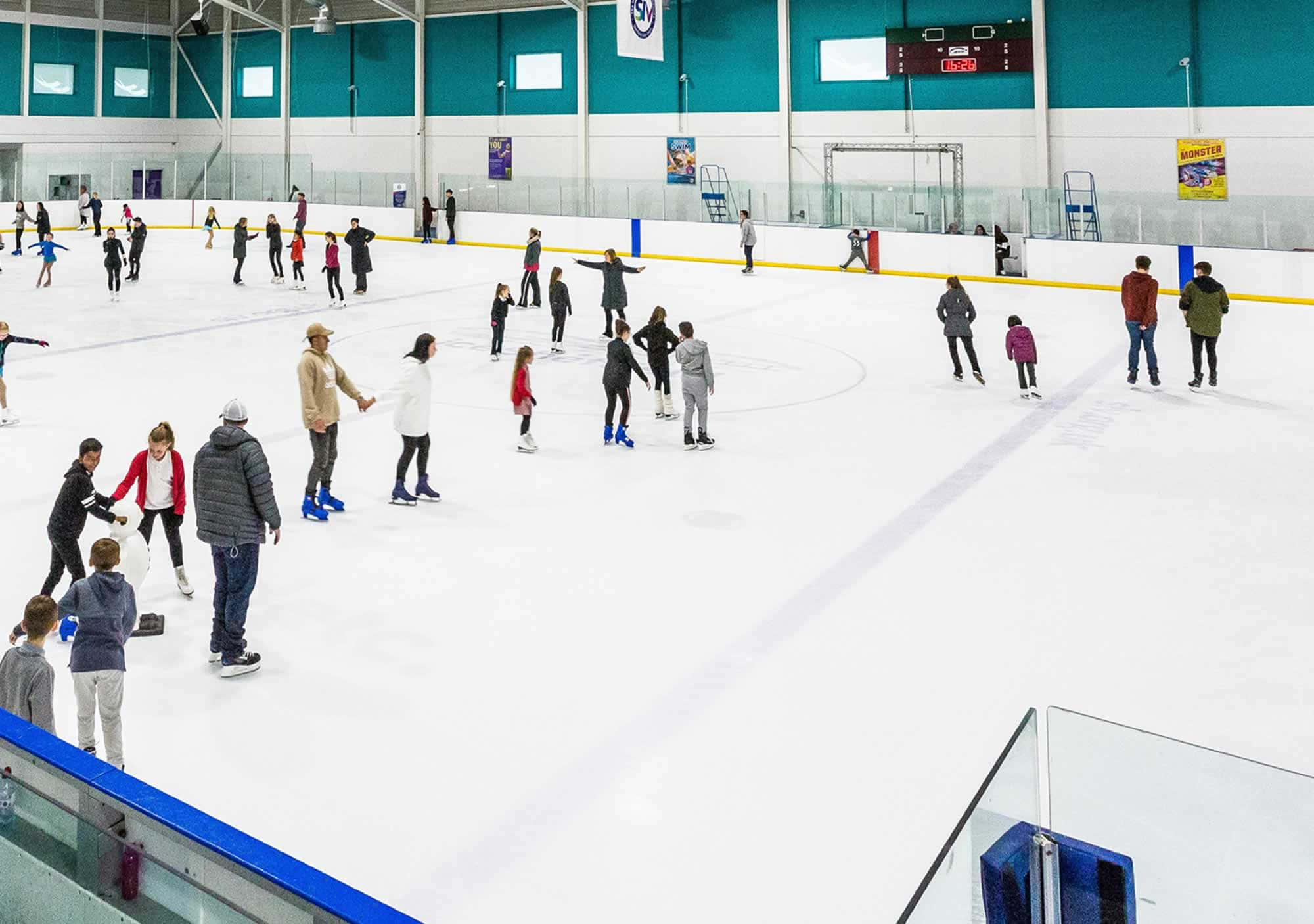 skating 桌布 壁紙 — 不同年齡的人在高天花板和青綠色牆壁的明亮室內溜冰場上滑行和學習。