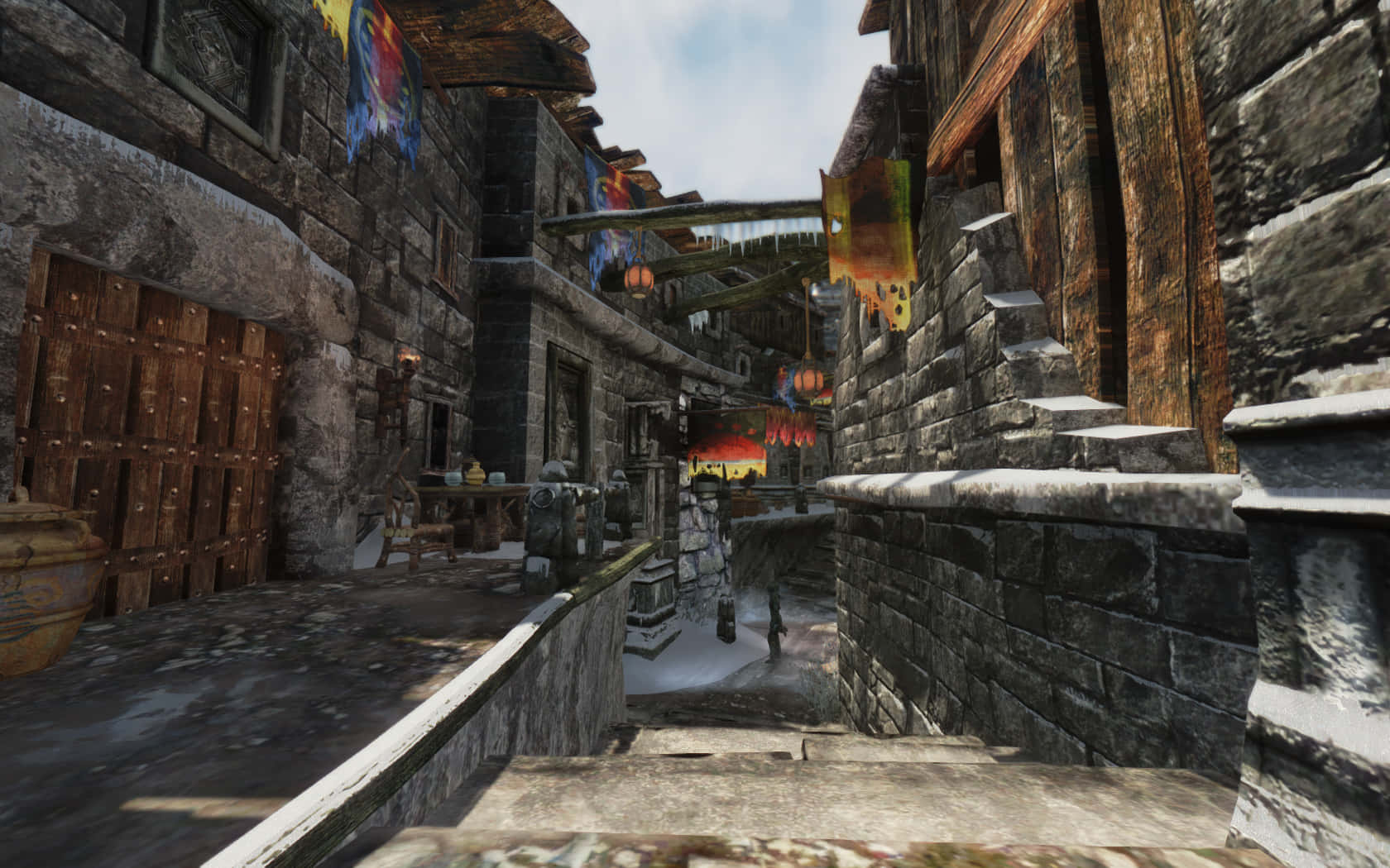 Skyrim Windhelm 桌布 壁紙 — 中世紀奇幻小鎮中的狹窄石頭小巷，木造建築、彩色旗幟，以及一個孤獨的身影走向泛紅的夕陽。