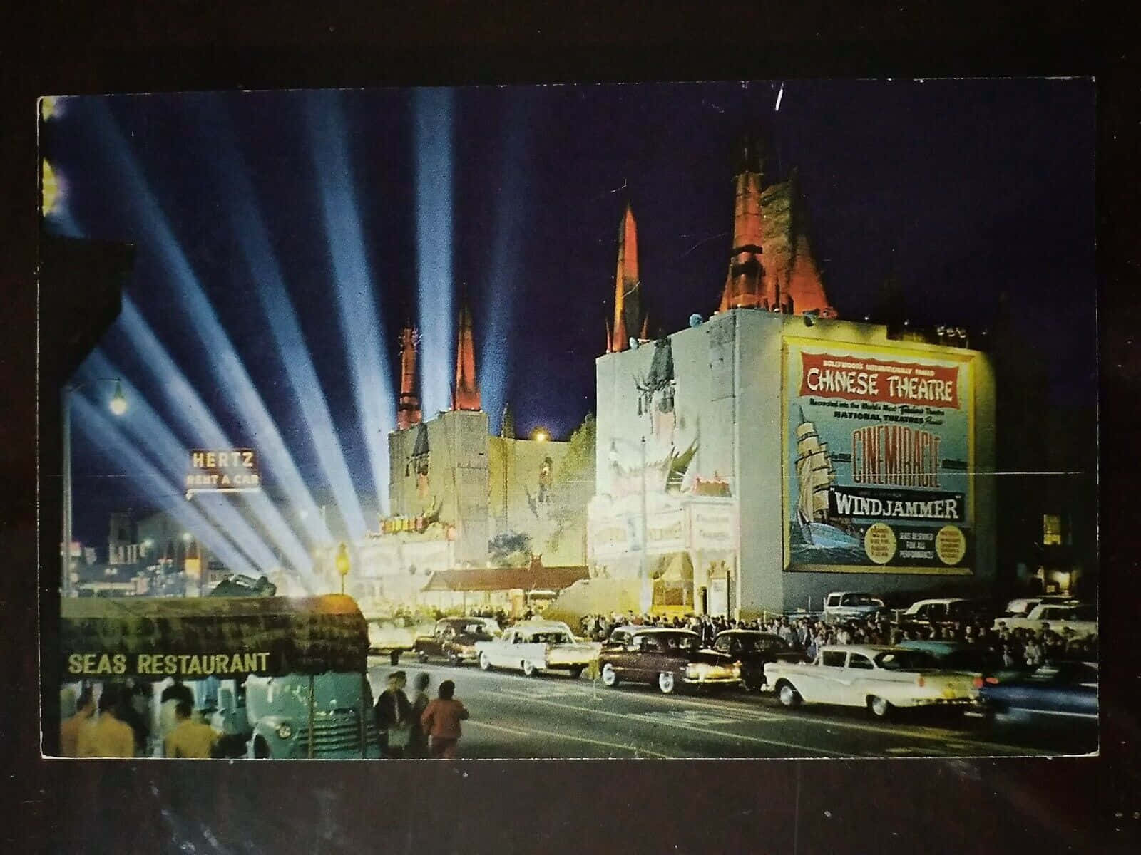 hollywood street 桌布 壁紙 — 中國戲院前的復古夜景，明亮的聚光燈、經典汽車和人群聚集在一張巨大的電影海報前。