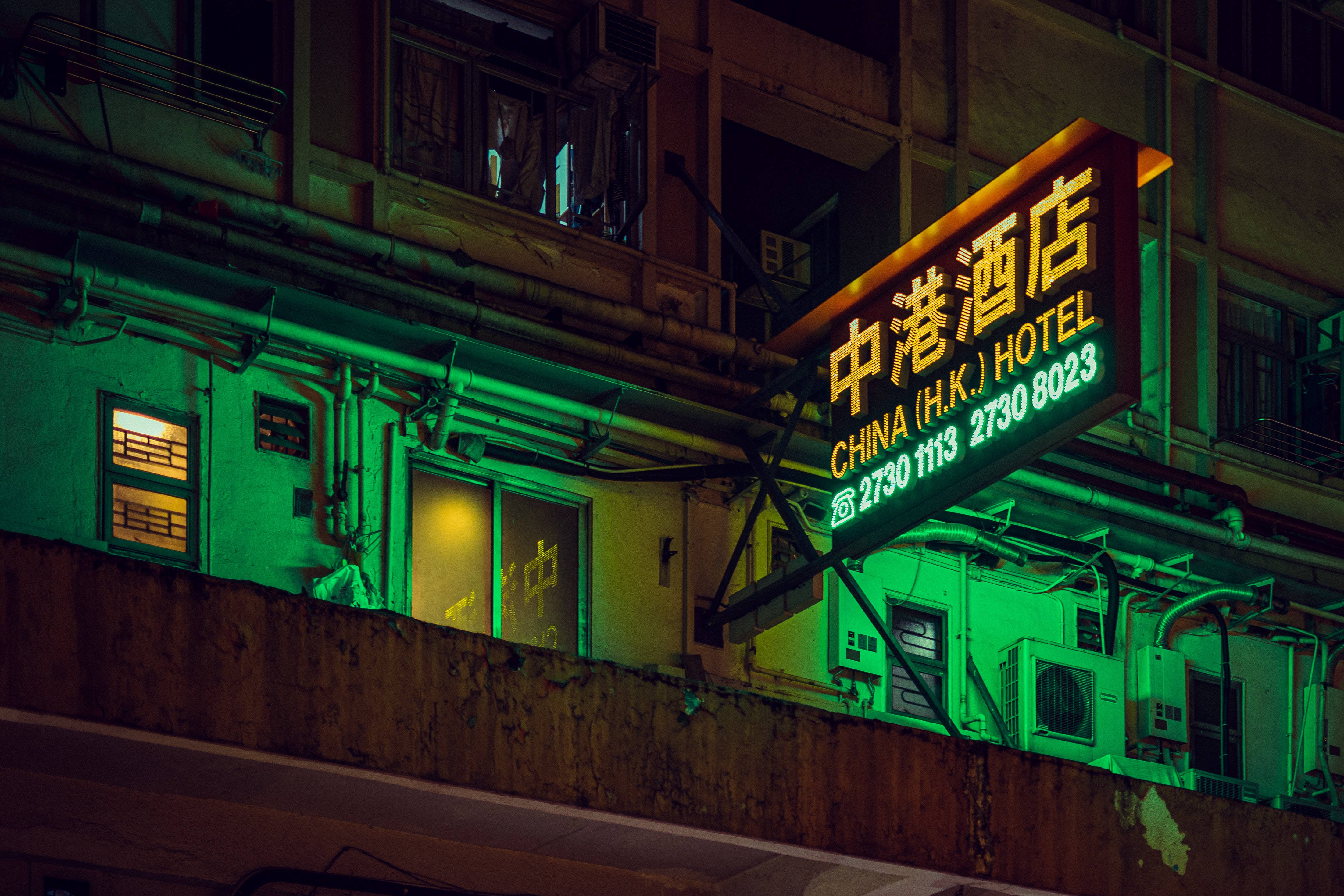 Hotel 桌布 壁紙 — 中國香港酒店閃爍的霓虹燈招牌在夜晚將鮮豔的綠光投射在風化的城市建築上。