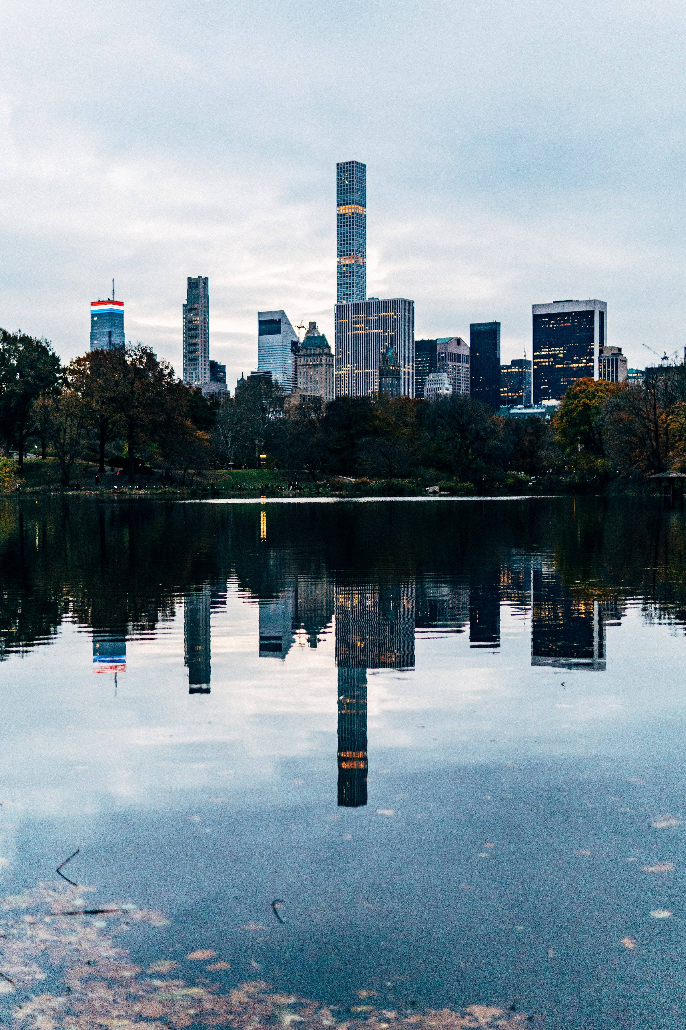 Lake 桌布 壁紙 — 中央公園一個寧靜的湖泊，在陰天和秋樹的映襯下，倒映著曼哈頓高聳的摩天大樓。