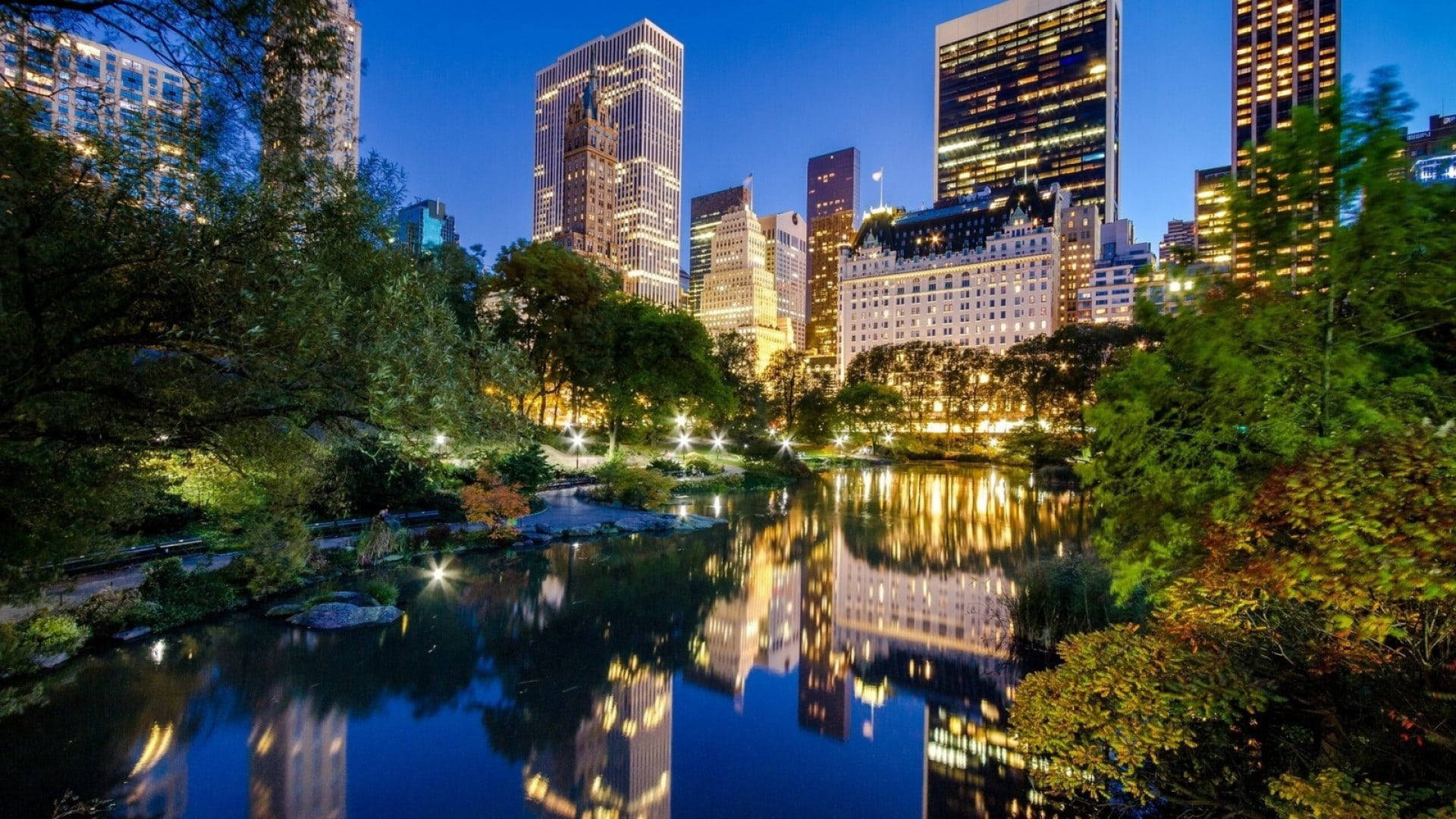 New 桌布 壁紙 — 中央公園寧靜的黃昏景色，摩天大樓倒映在平靜的池塘中，四周環繞著茂密的樹木。