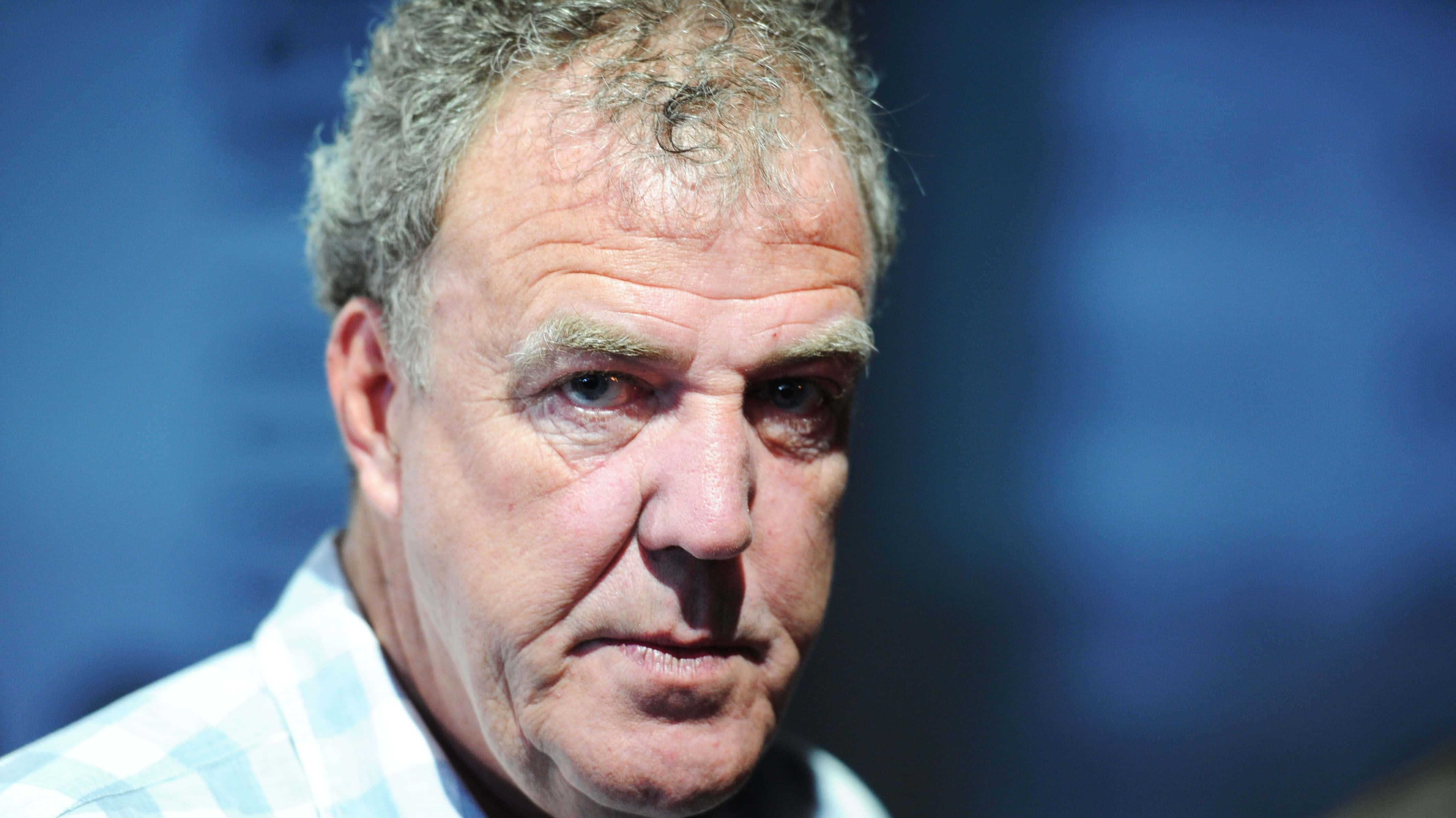 Jeremy Clarkson 桌布 壁紙 — 中年嚴肅男子特寫肖像，頭髮花白，眼神銳利，背景為模糊的藍色。