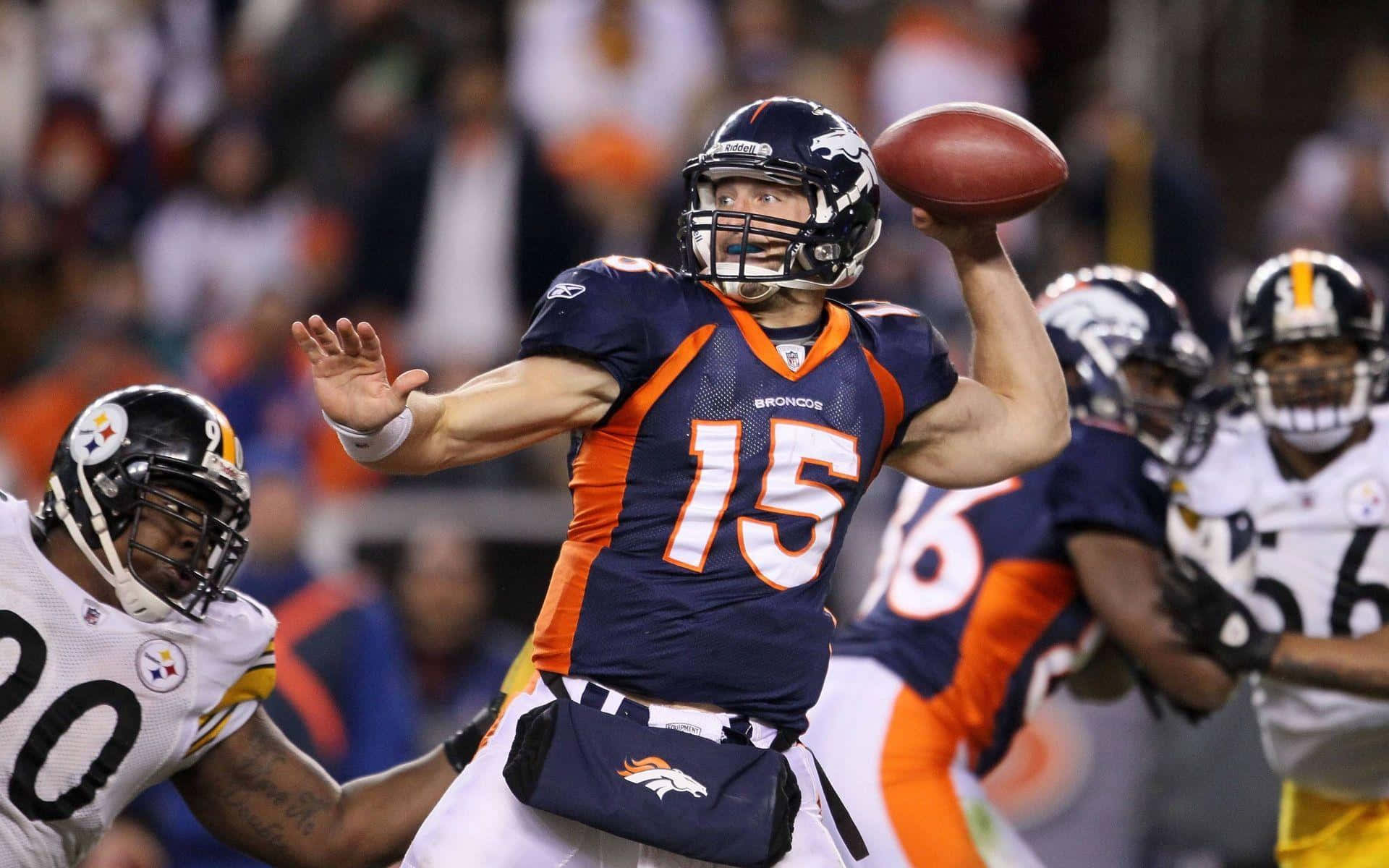 Tim Tebow 桌布 壁紙 — 丹佛野馬隊的四分衛身穿藍色和橙色球衣，在夜間比賽中防守球員逼近時擲出橄欖球。