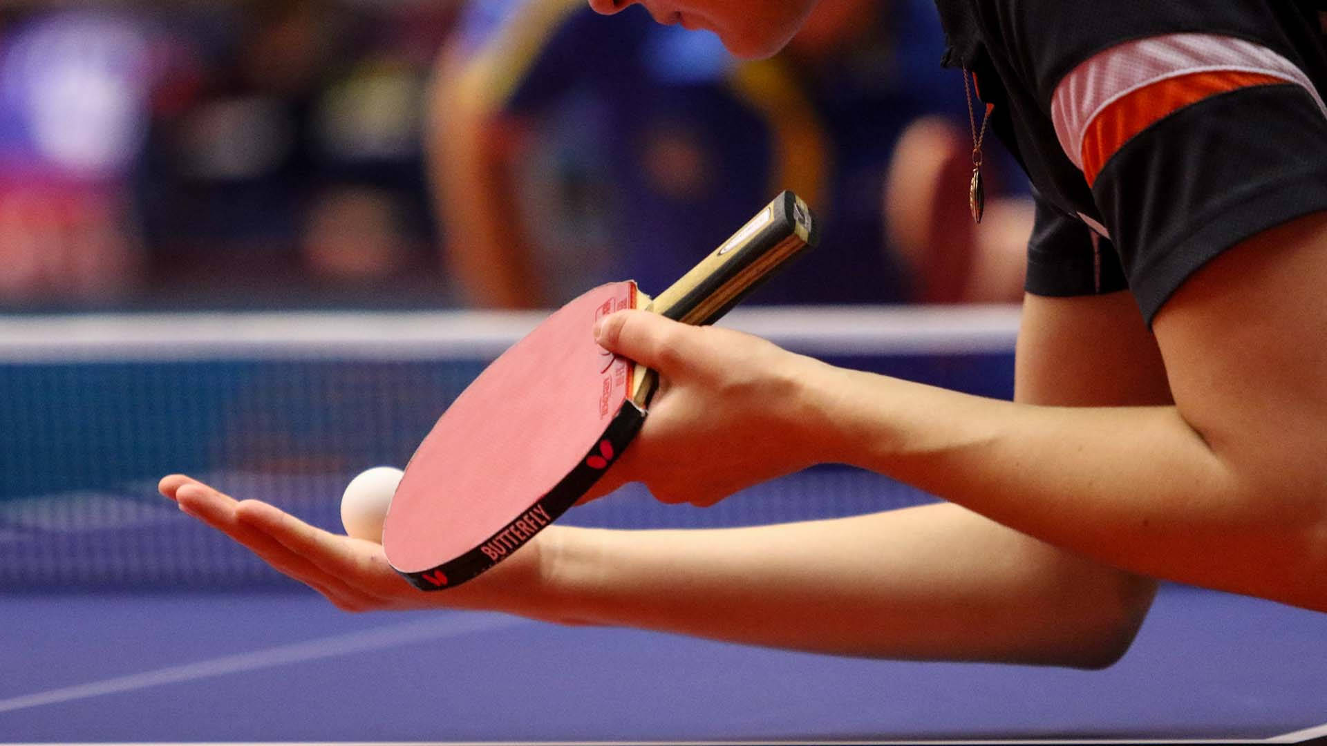 Table Tennis 桌布 壁紙 — 乒乓球運動員在藍色球場上手持球拍和球準備發球的特寫。