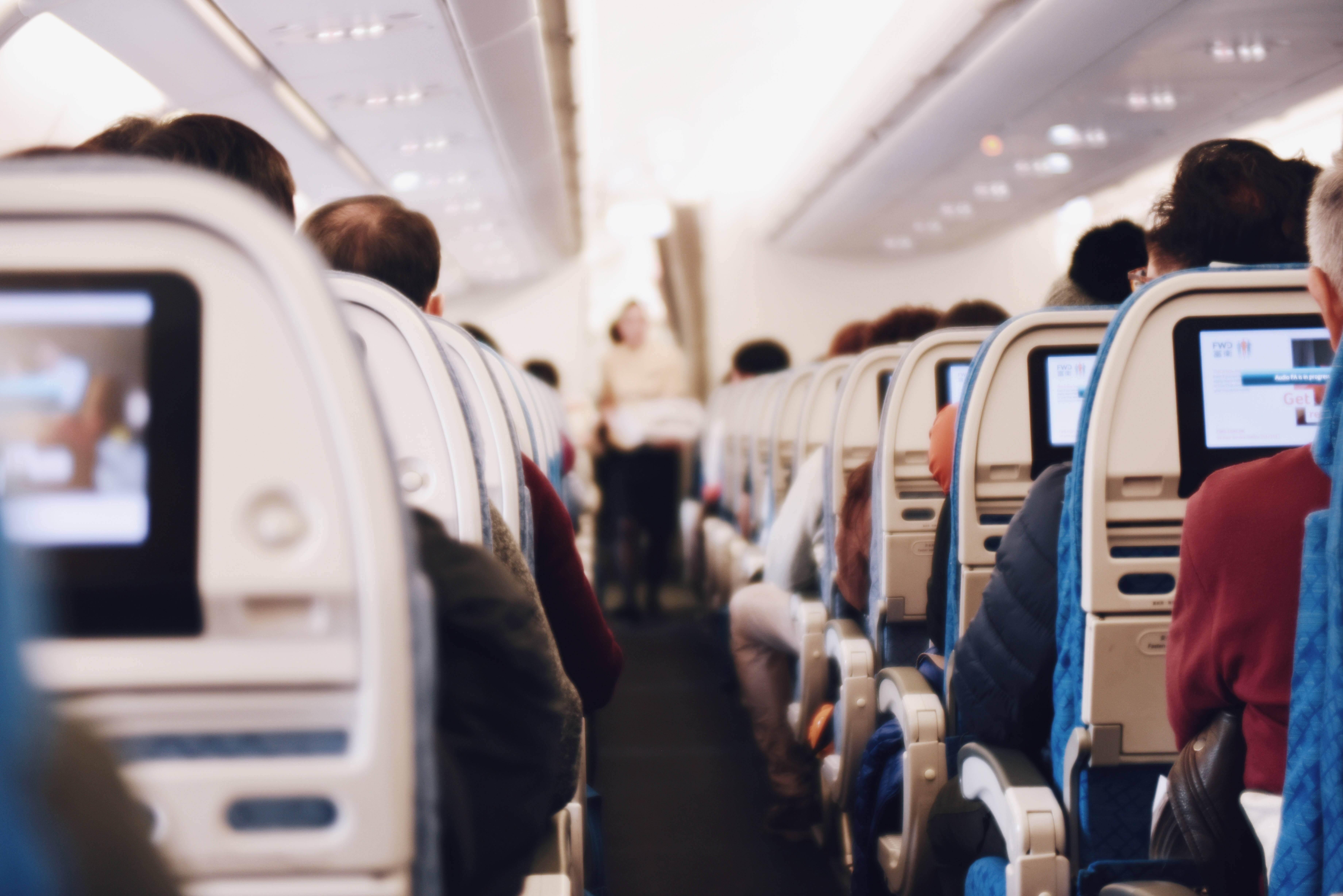飛機 桌布 壁紙 — 乘客坐在一排排飛機座位上，個人螢幕發光，空中服務員正走過通道。