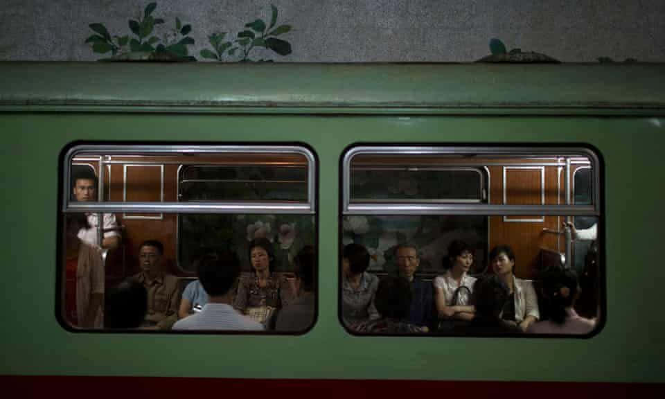 North Korea 桌布 壁紙 — 乘客坐在光線昏暗的綠色火車車廂內，透過窗戶看到上方有植物生長。