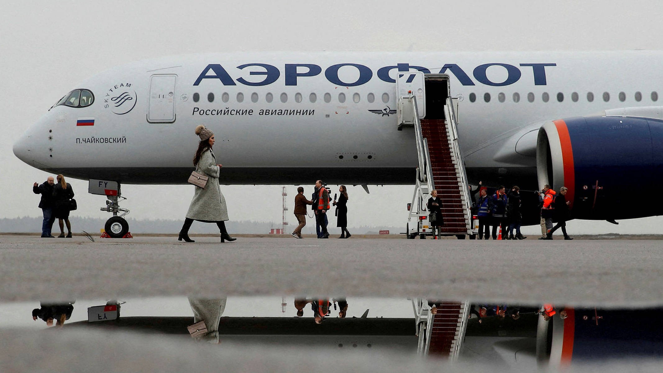 Airport 桌布 壁紙 — 乘客從俄羅斯Aeroflot飛機下機，停在濕滑的停機坪上，水坑在陰天天空下反射出場景。