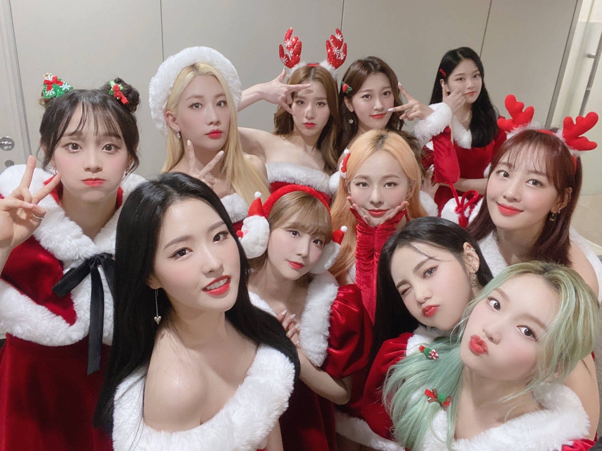 Santa 桌布 壁紙 — 九位年輕女性身穿節日紅白聖誕老人服裝，在室內戴著馴鹿角，表情俏皮，愉快地擺姿勢。