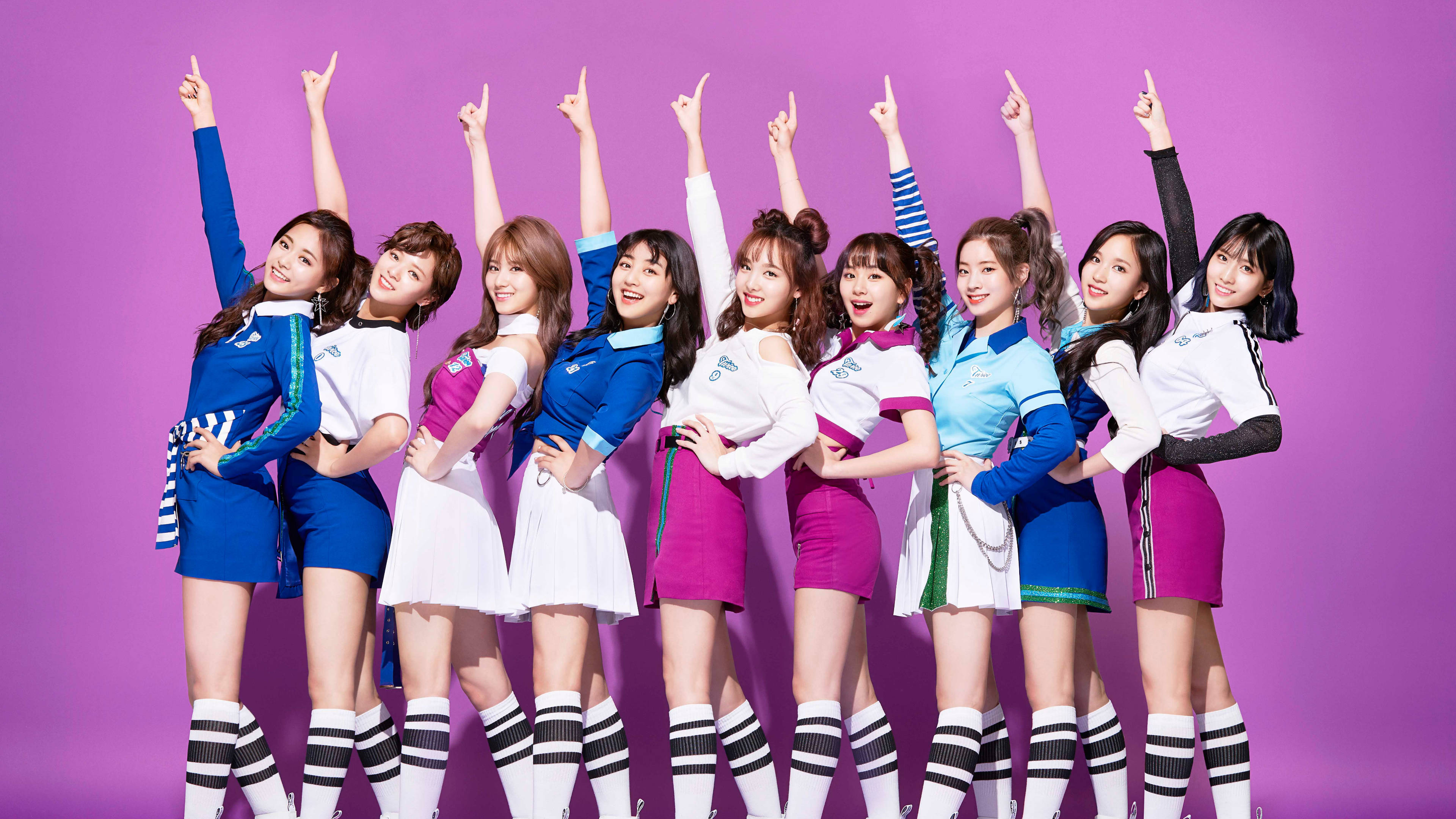 Kpop Aesthetic 桌布 壁紙 — 九位微笑的女性偶像穿著協調的藍色和粉紅色服裝，在純紫色背景前舉起手臂擺姿勢。