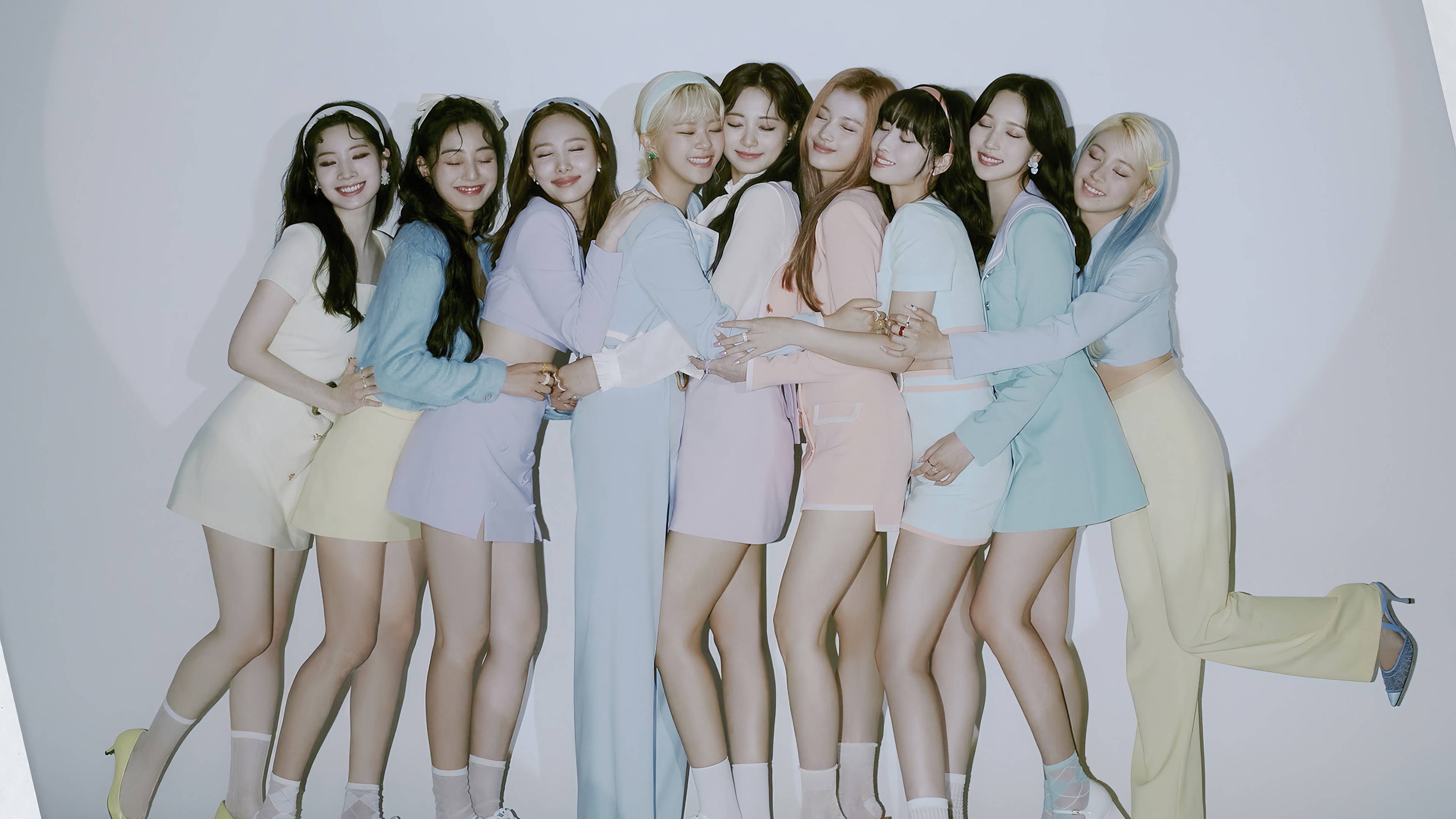 Kpop Aesthetic 桌布 壁紙 — 九位微笑的年輕女性穿著柔和色調的服裝，在純白背景前緊密地靠在一起。