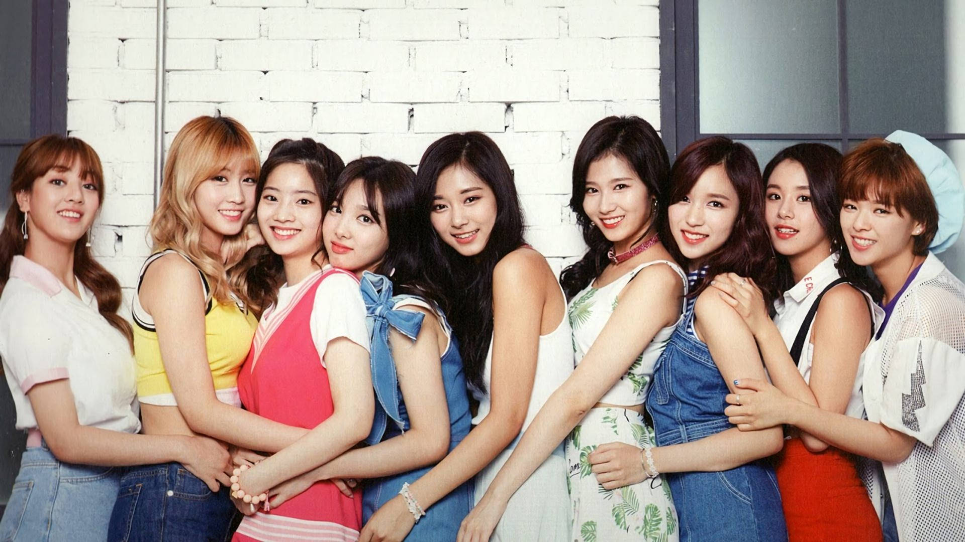 twice 桌布 壁紙 — 九位微笑的年輕女性穿著色彩繽紛的休閒服裝，緊密地靠在一起，以白色磚牆為背景擺姿勢。