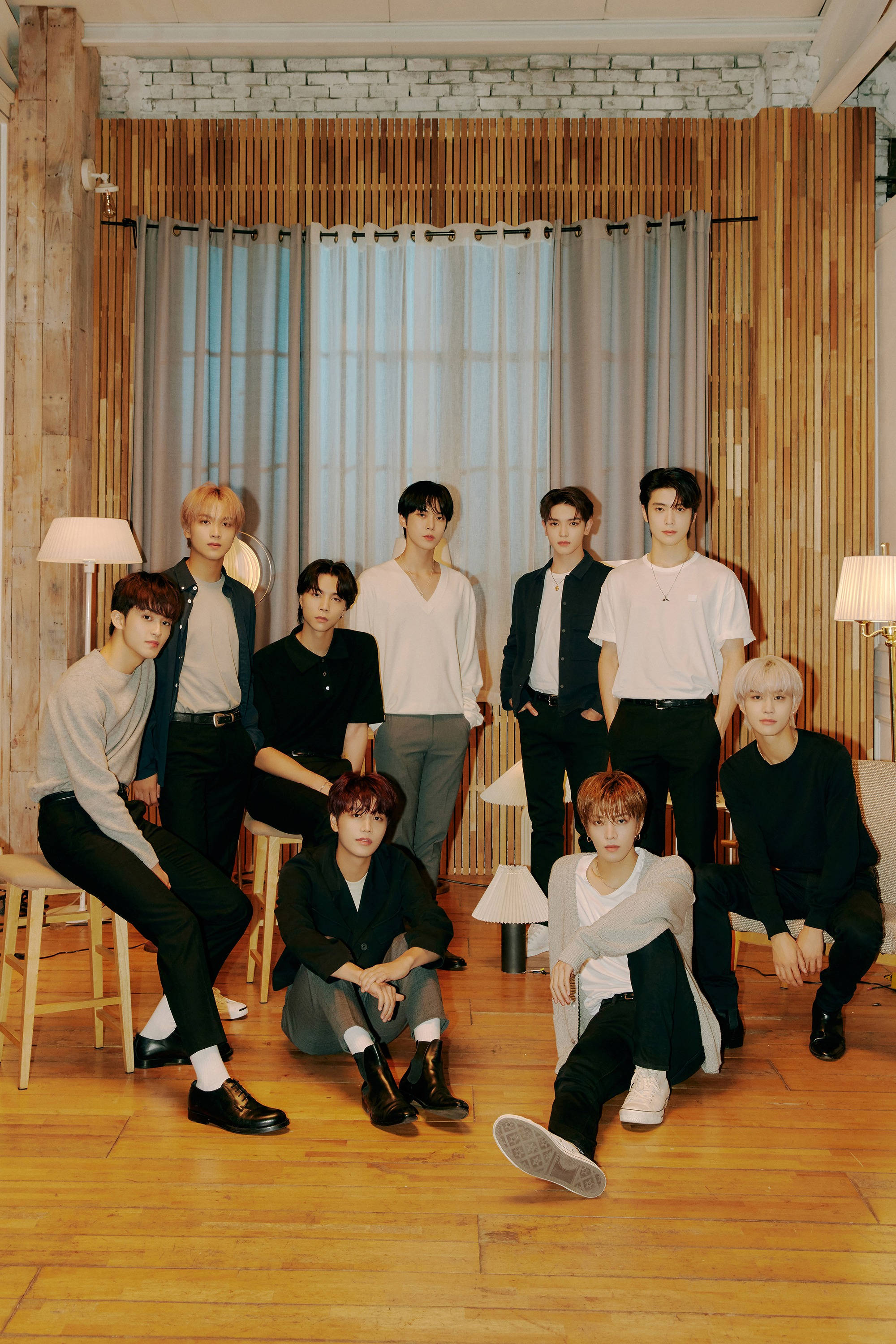 Nct 桌布 壁紙 — 九位時尚年輕男士在一個現代木質房間內隨意擺姿勢，房間有磚牆和落地燈。