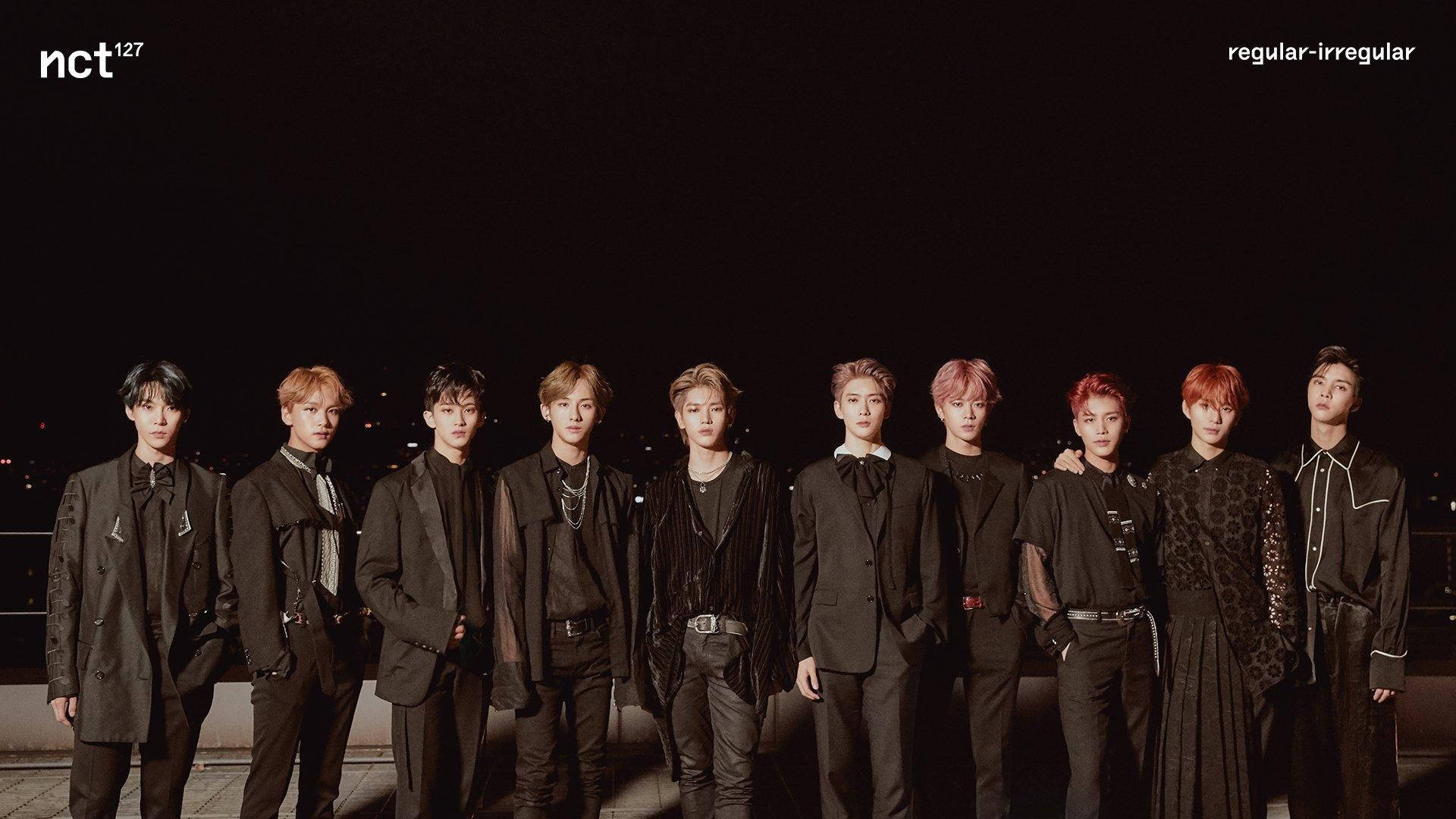 Ateez Desktop 桌布 壁紙 — 九位時尚年輕男士身穿深色西裝，在夜間城市天際線背景下自信地擺姿勢。