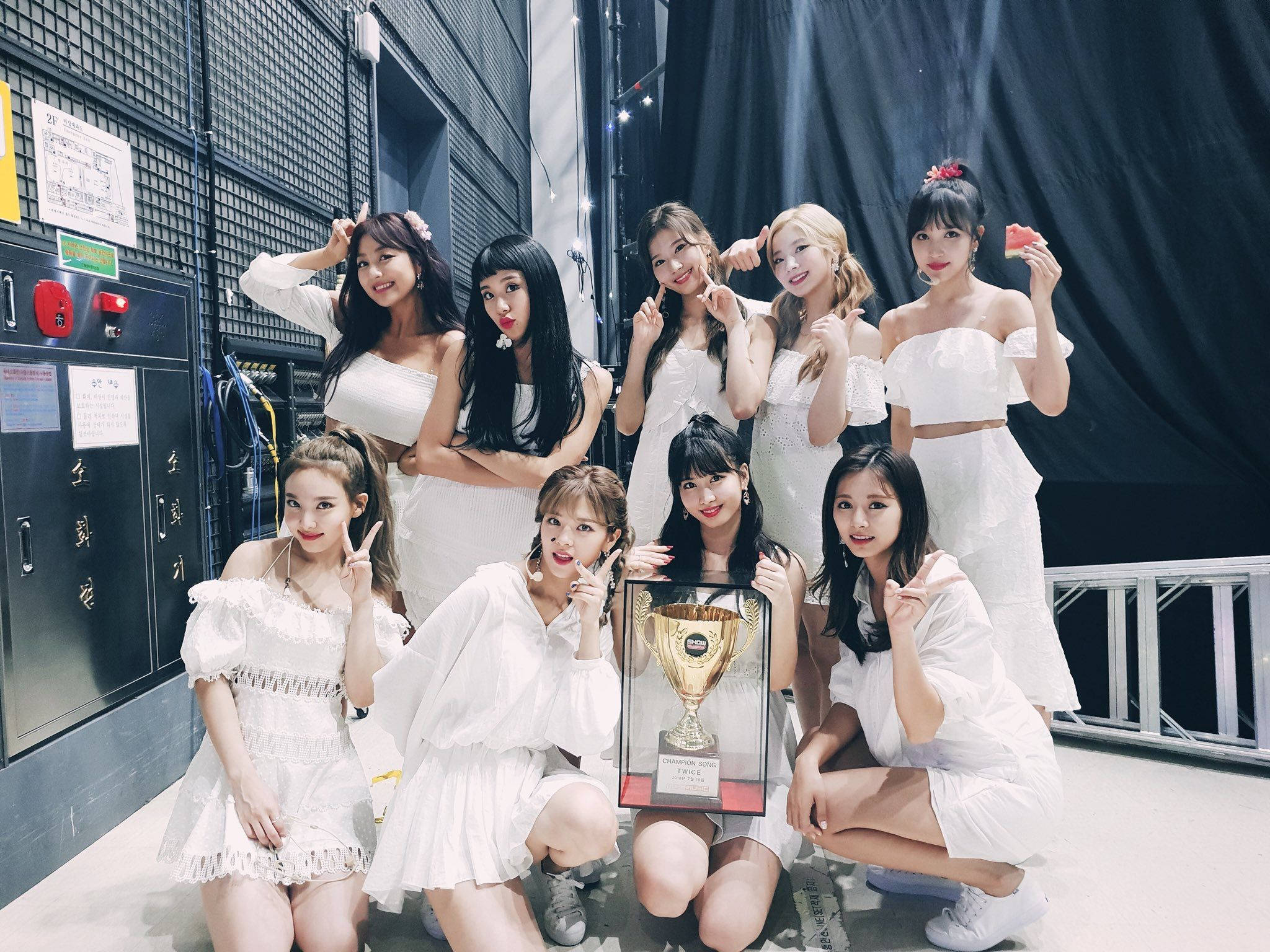 twice 桌布 壁紙 — 九位身穿白色服裝的女性在後台工作室環境中圍著一個金色獎盃愉快地擺姿勢。