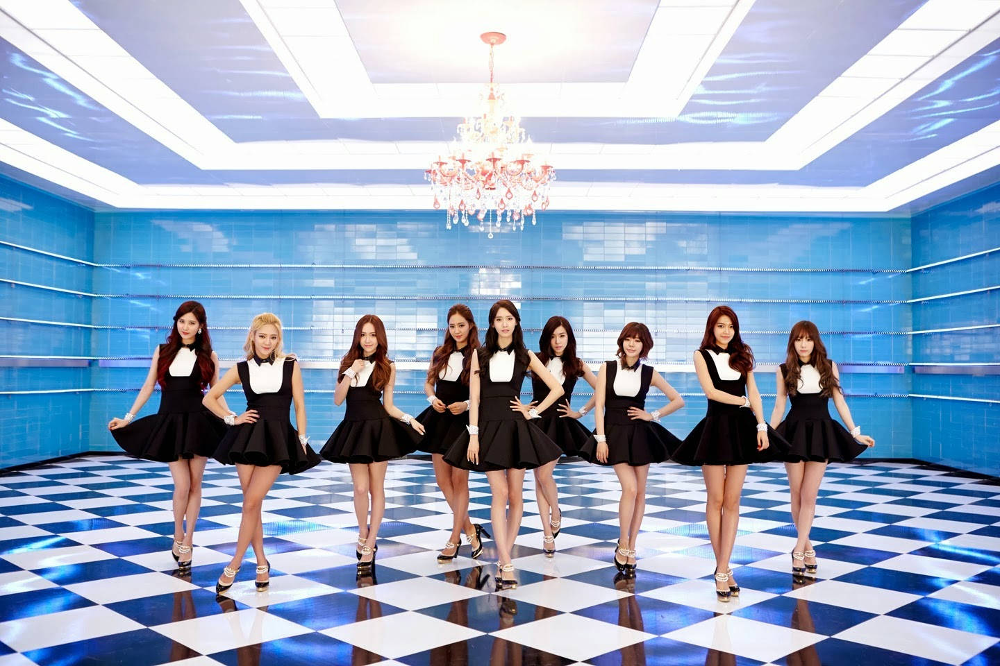 K Pop 桌布 壁紙 — 九位身穿黑白服裝的女性，在未來感藍色房間的水晶吊燈下，自信地站在藍白格子地板上。
