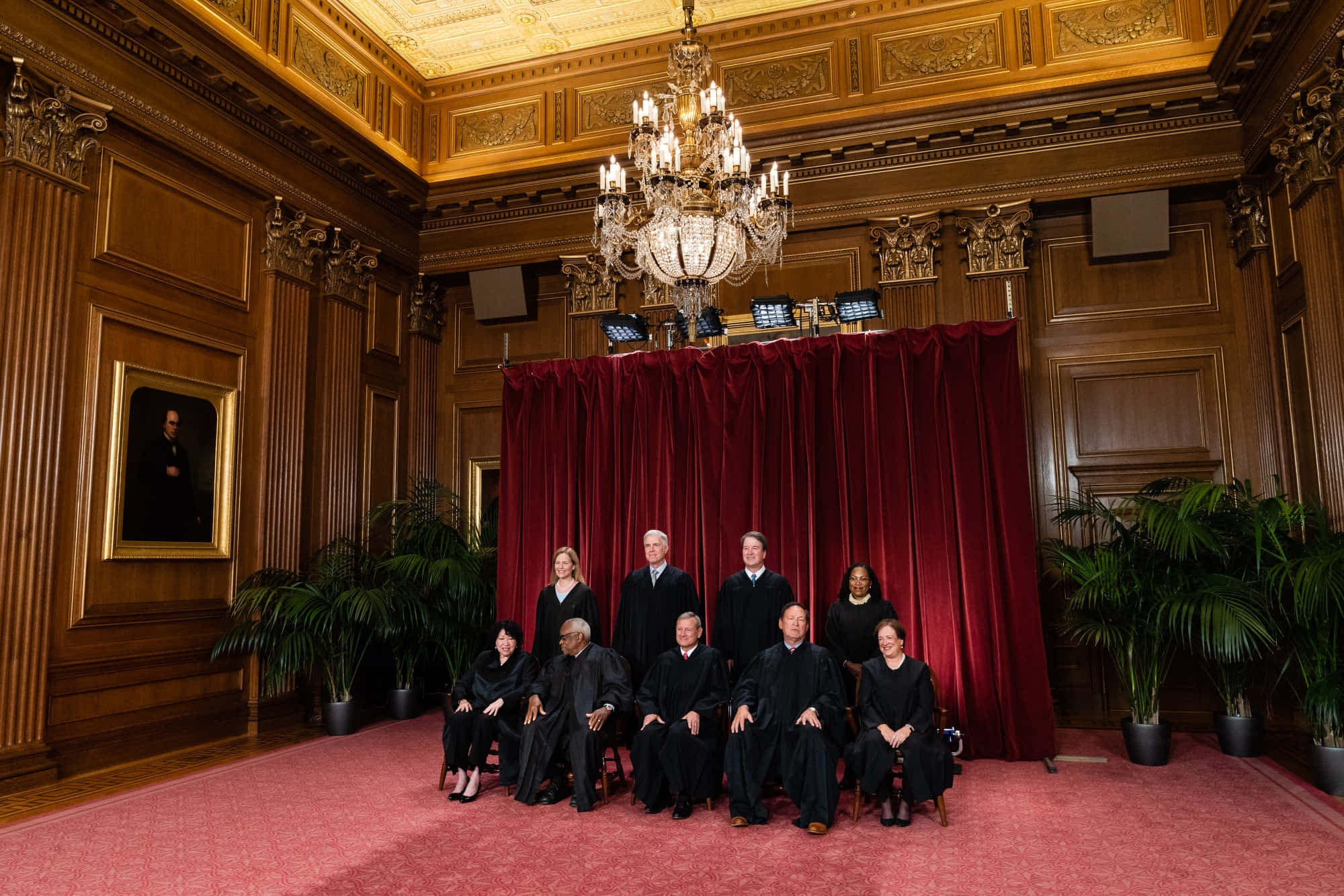Supreme Court 桌布 壁紙 — 九位身穿黑色長袍的法官在一個裝有吊燈的宏偉木鑲板法庭中，在紅色窗簾前正式擺姿勢。