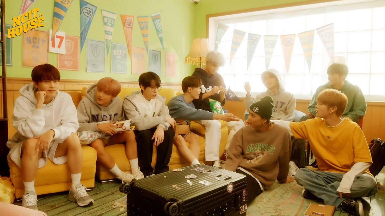Nct 桌布 壁紙 — 九個穿著休閒服的年輕男子放鬆地坐在黃色沙發和地板上，房間光線充足，裝飾著彩色三角旗。