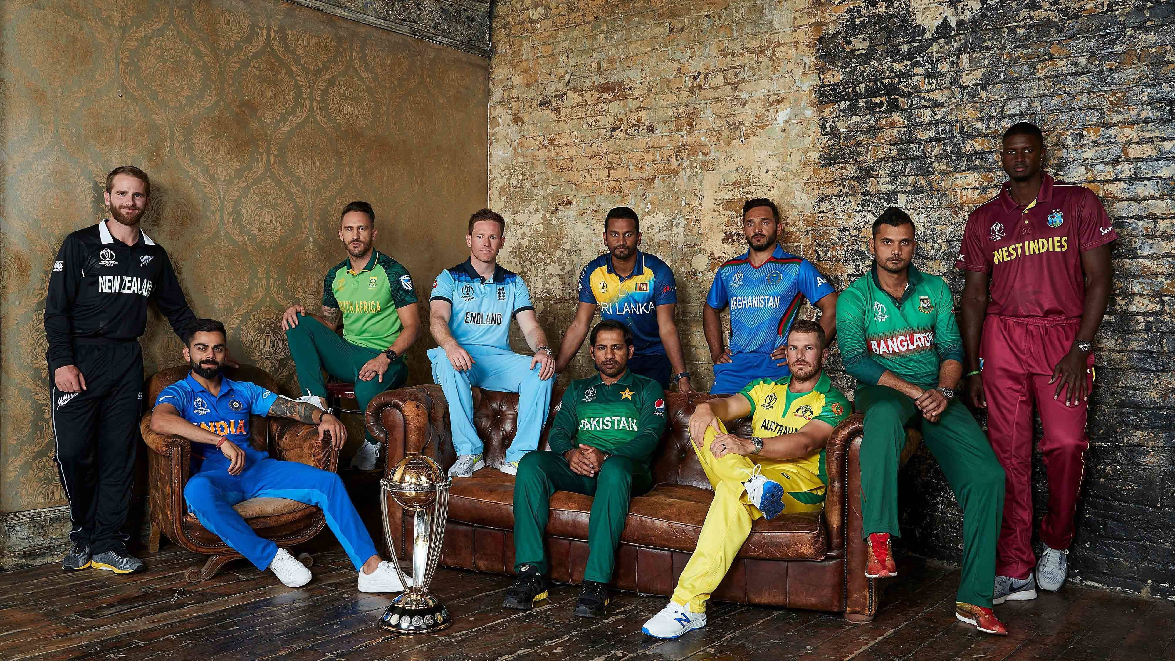 England Cricket 桌布 壁紙 — 九名板球運動員身穿國家隊制服，在皮革沙發上自信地圍繞獎盃擺姿勢，背景是質樸的磚牆。