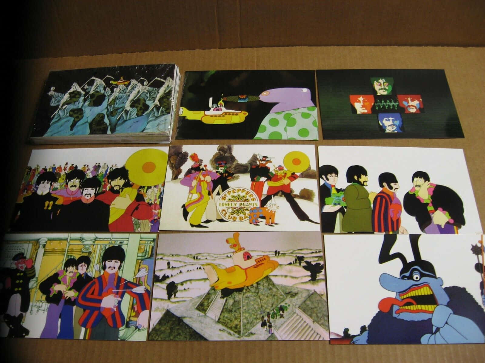 Yellow Submarine 桌布 壁紙 — 九張標誌性的披頭四專輯封面藝術品排列在一個紙板箱中，展示迷幻插圖和超現實場景。