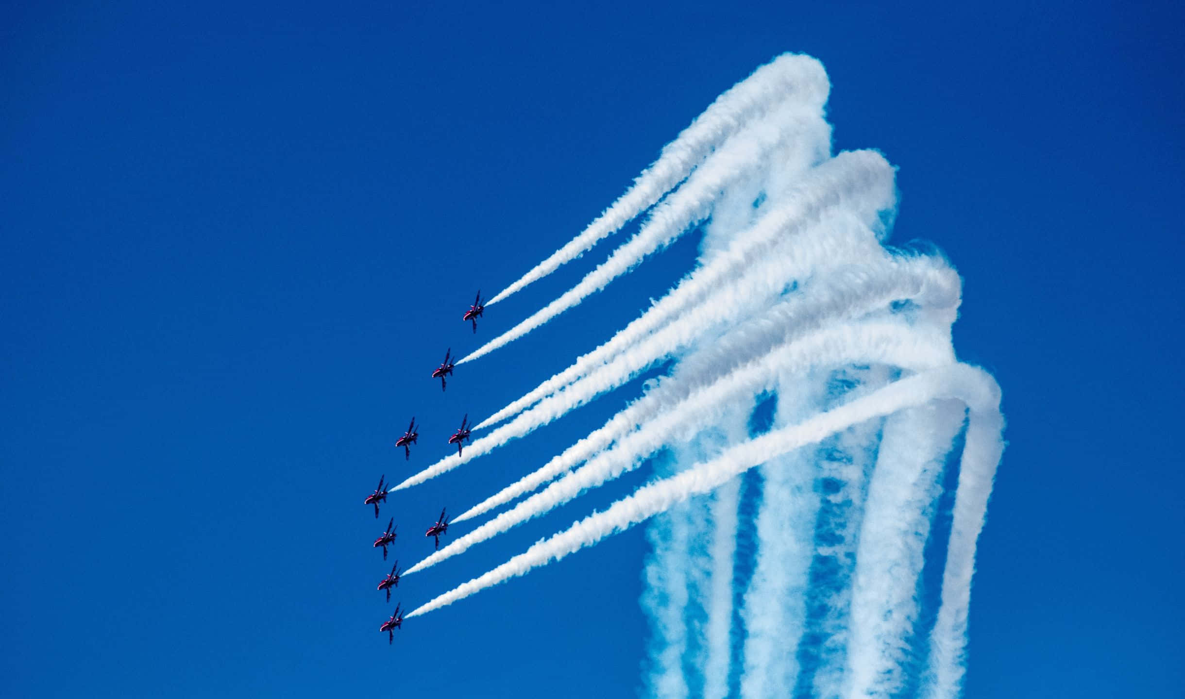 2440x1440 Small Planes 桌布 壁紙 — 九架紅色噴射機在晴朗的藍天下以緊密編隊飛行，留下濃厚的白色煙霧痕跡。