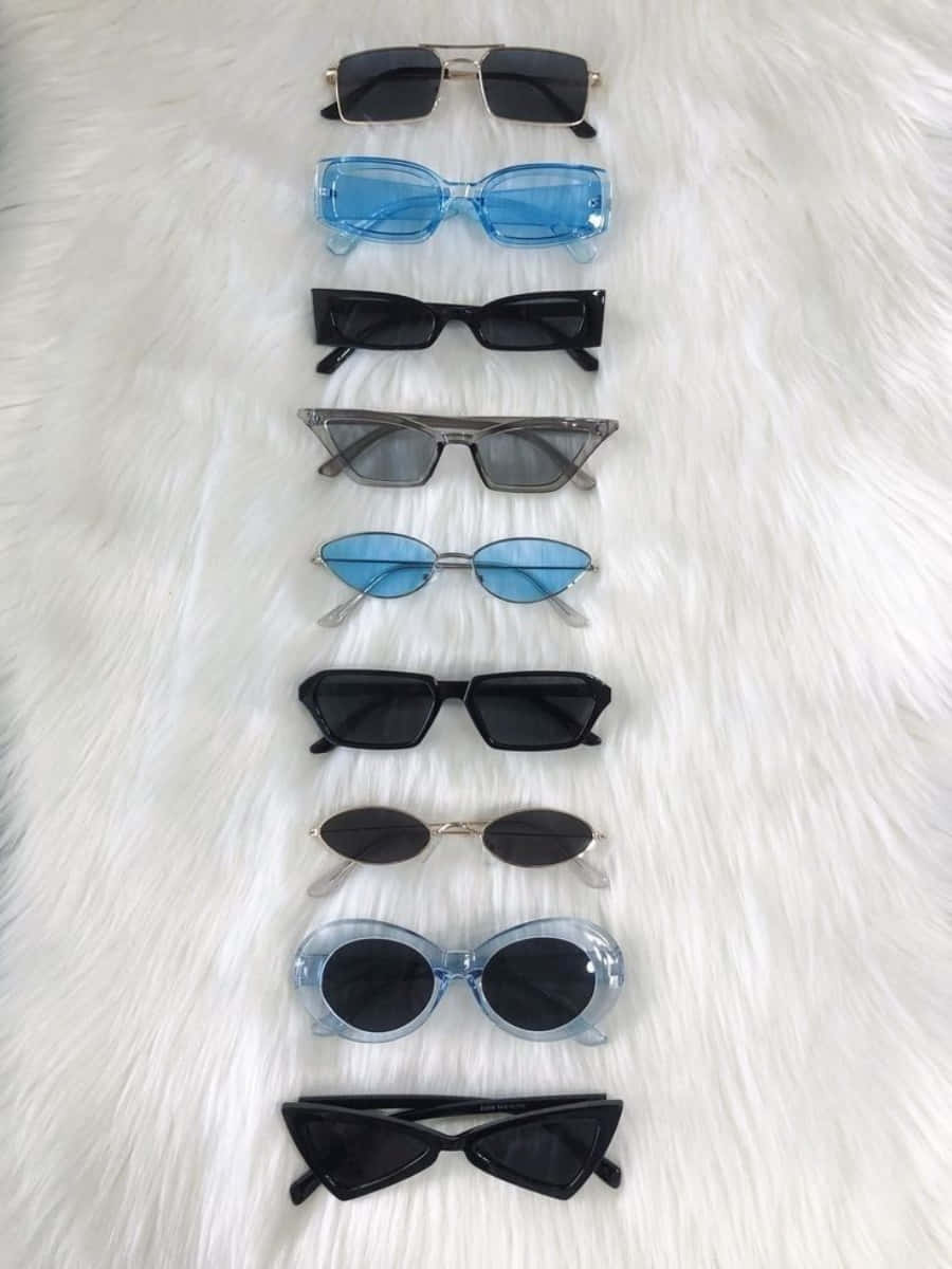Sunglasses 桌布 壁紙 — 九款時尚太陽眼鏡，形狀和顏色各異，整齊地排列在柔軟的白色毛絨表面上。