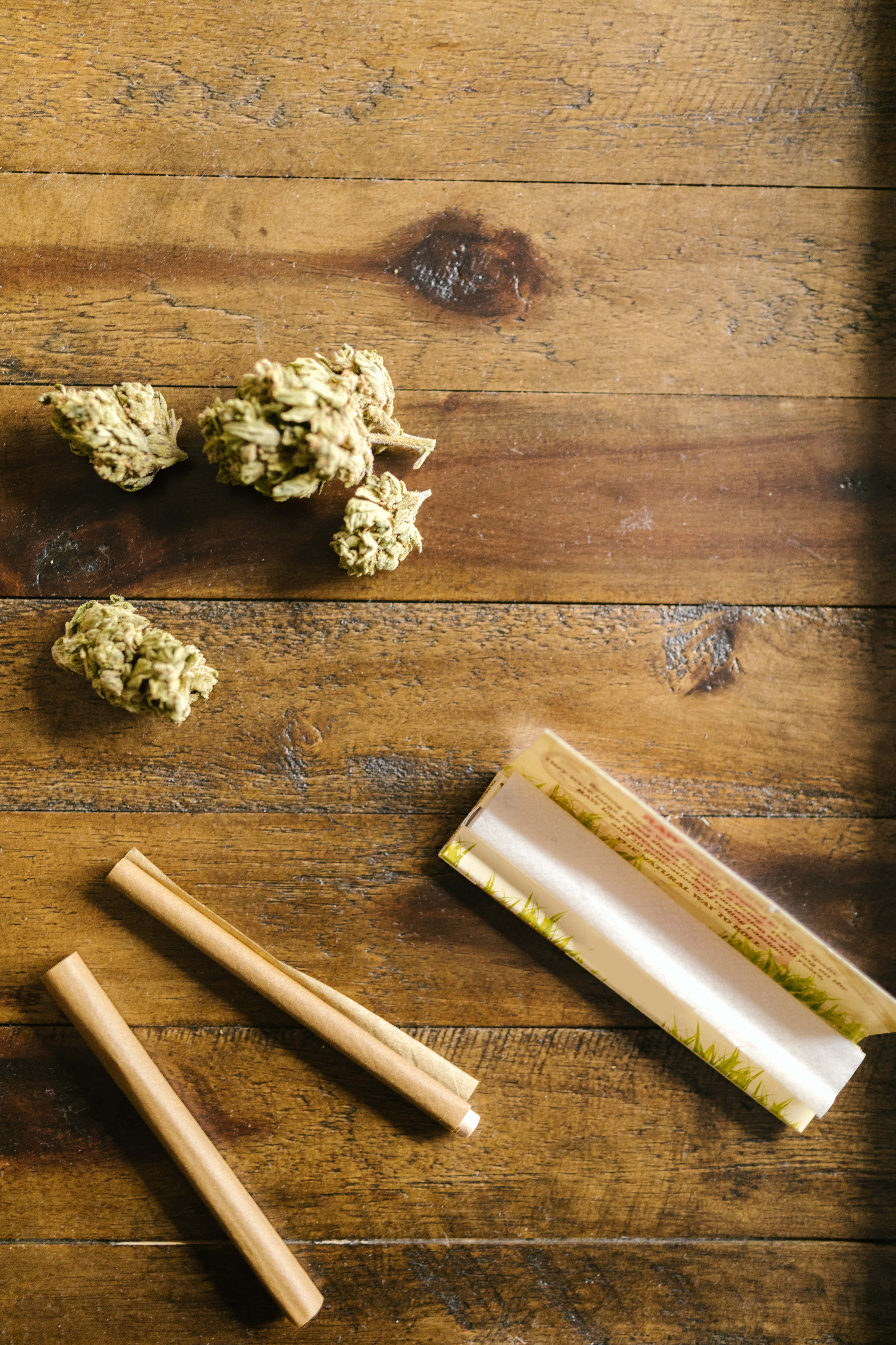 大麻 桌布 壁紙 — 乾燥大麻花蕾和捲菸紙放在經風化的木質表面上，伴隨溫暖的自然光線。