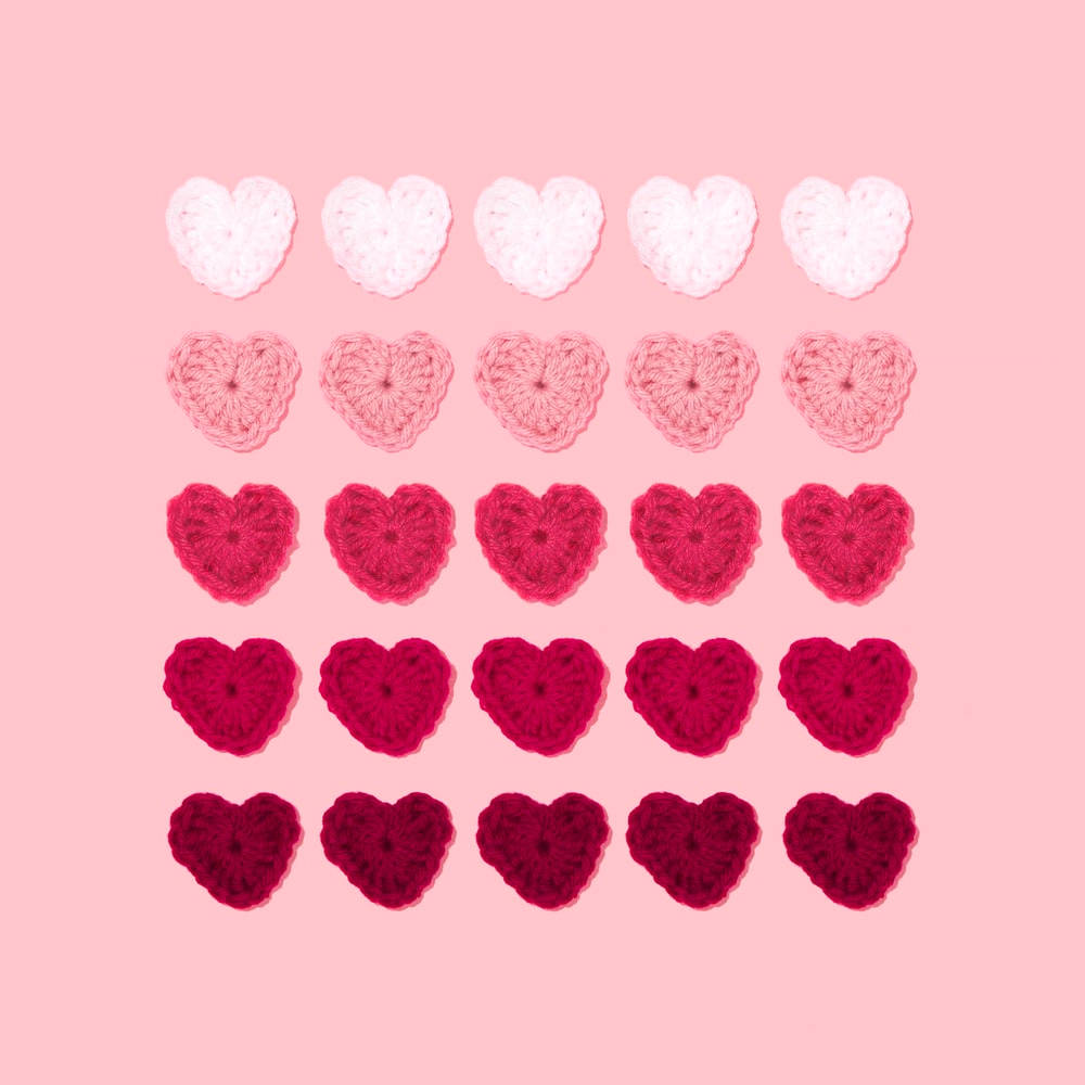 Pastel Pink Heart 桌布 壁紙 — 二十個鉤針編織的心形，採用漸變粉紅色調，整齊排列在柔和的粉紅色背景上。