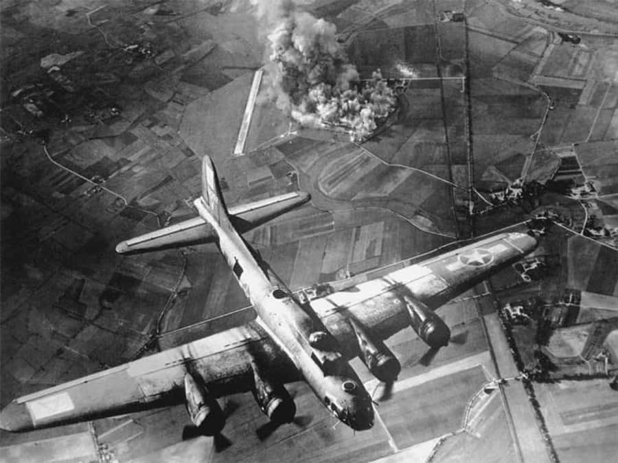 World War 2 桌布 壁紙 — 二戰轟炸機飛越鄉村景觀的鳥瞰圖，下方目標升起濃煙。