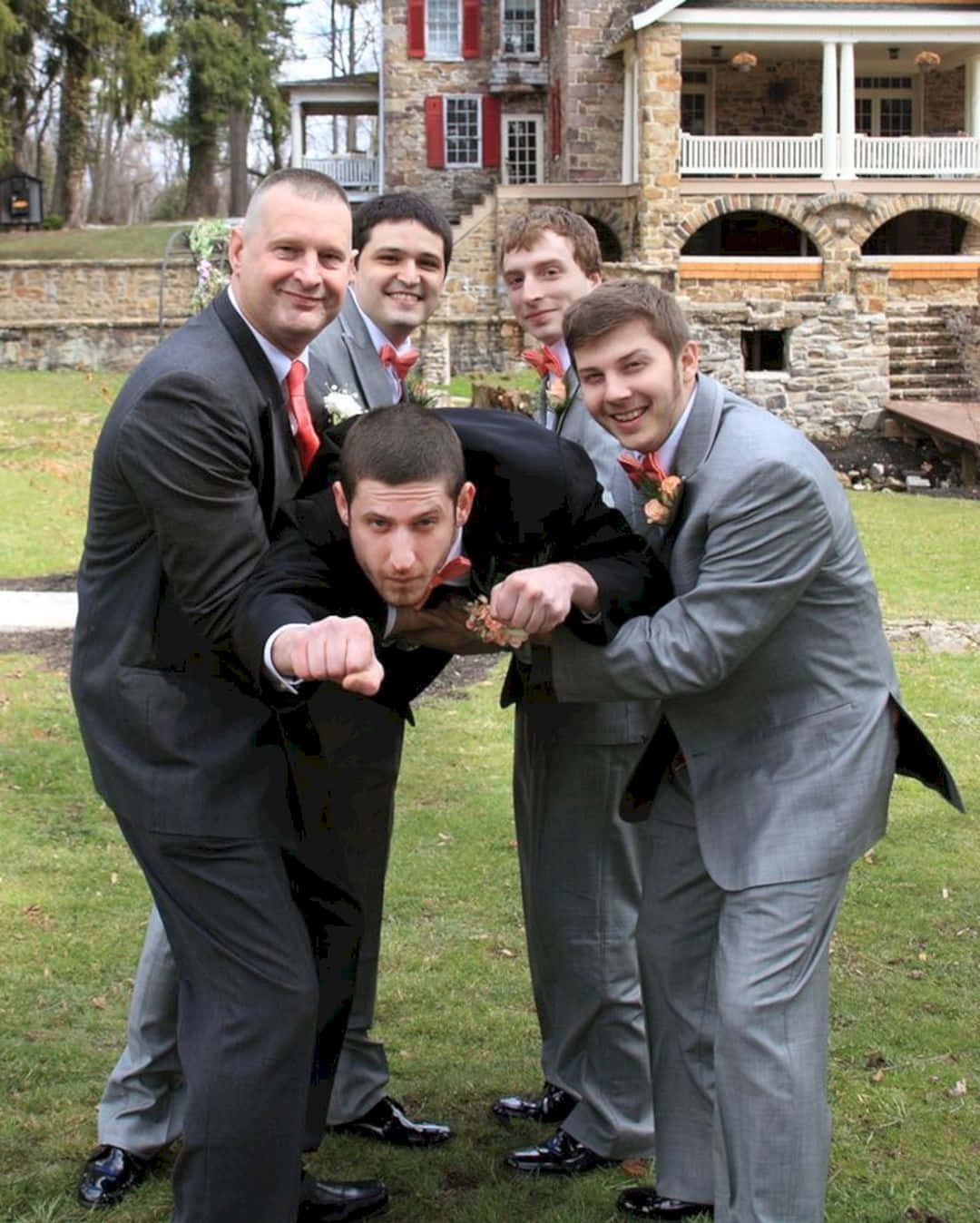 Groomsmen 桌布 壁紙 — 五位伴郎穿著西裝，在戶外以石砌大宅為背景，俏皮地擺姿勢。