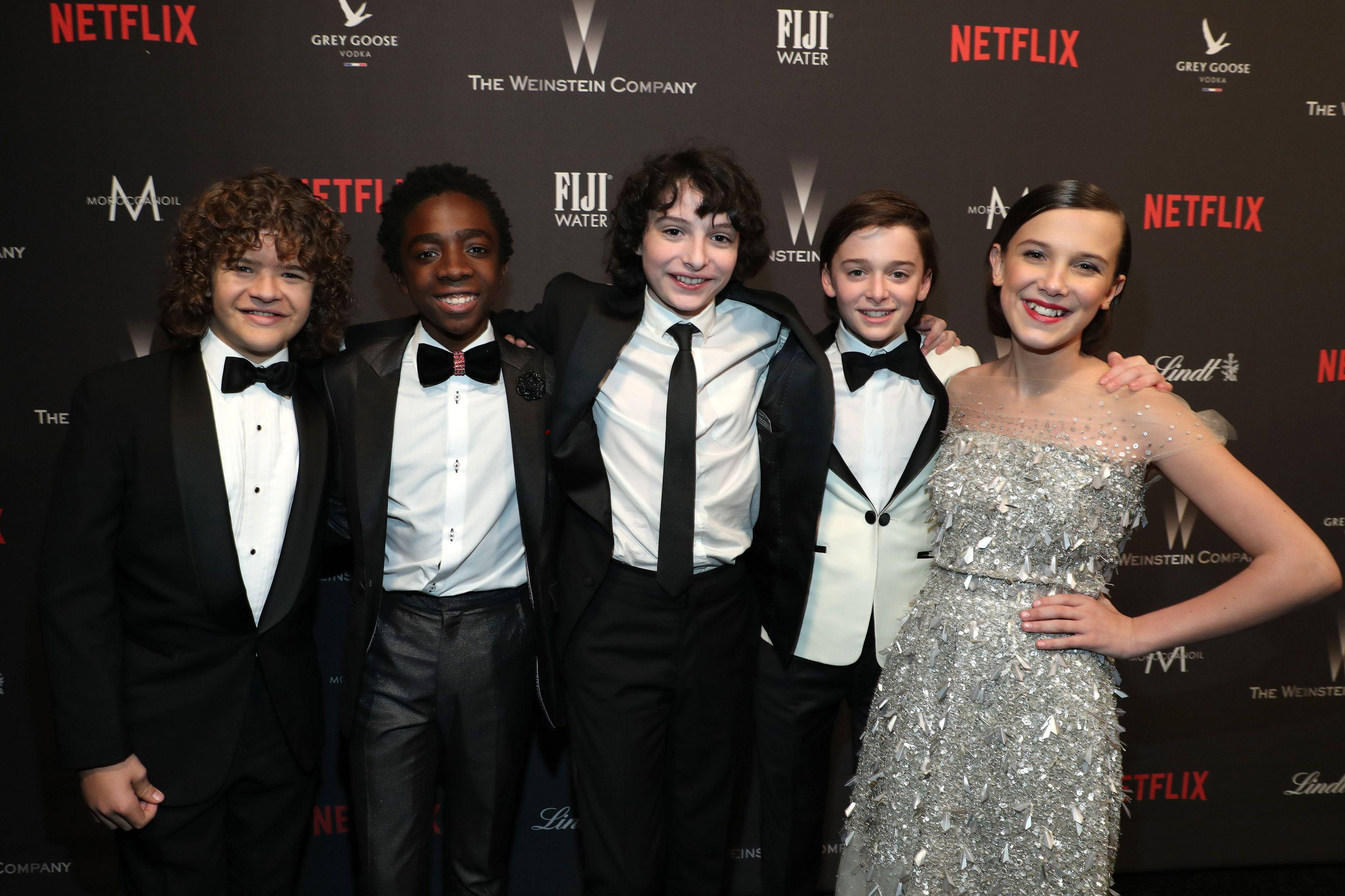 Cast 桌布 壁紙 — 五位年輕演員穿著正式服裝，在有品牌背景的紅地毯活動中一起擺姿勢。