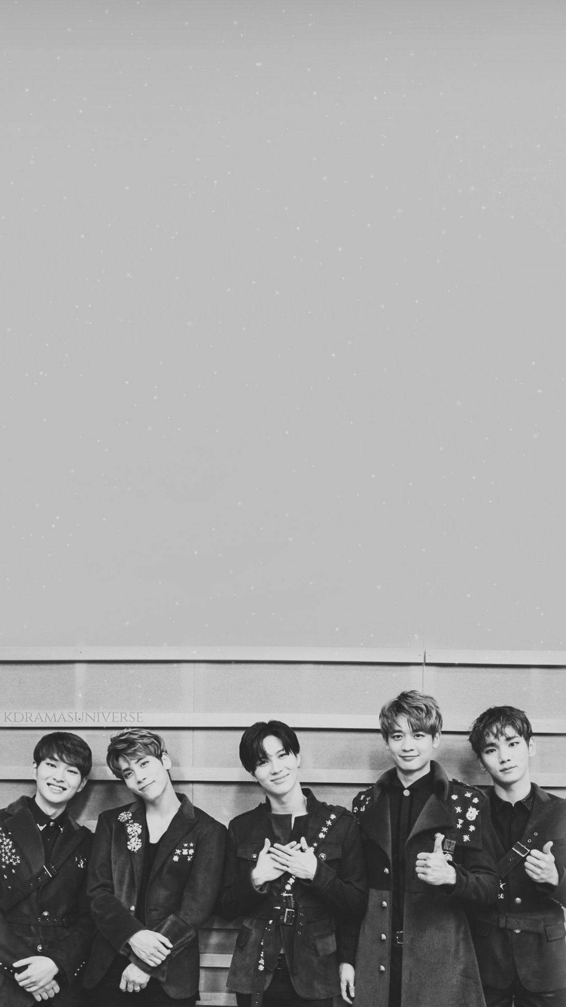 Shinee 桌布 壁紙 — 五位年輕男士身穿時尚黑色外套，在帶有細微紋理的簡約灰色牆壁前自信擺姿勢。