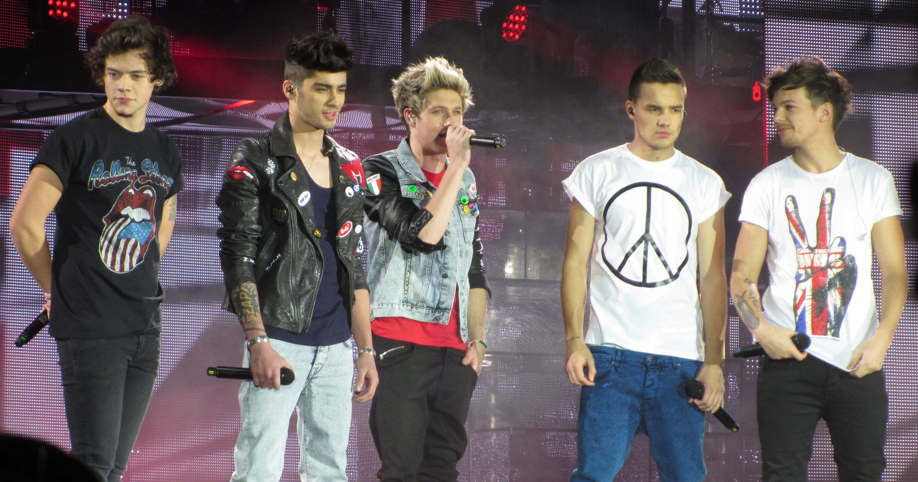 One Direction 桌布 壁紙 — 五位年輕男音樂家在燈光璀璨的舞台上表演，身後有LED螢幕和煙霧效果。