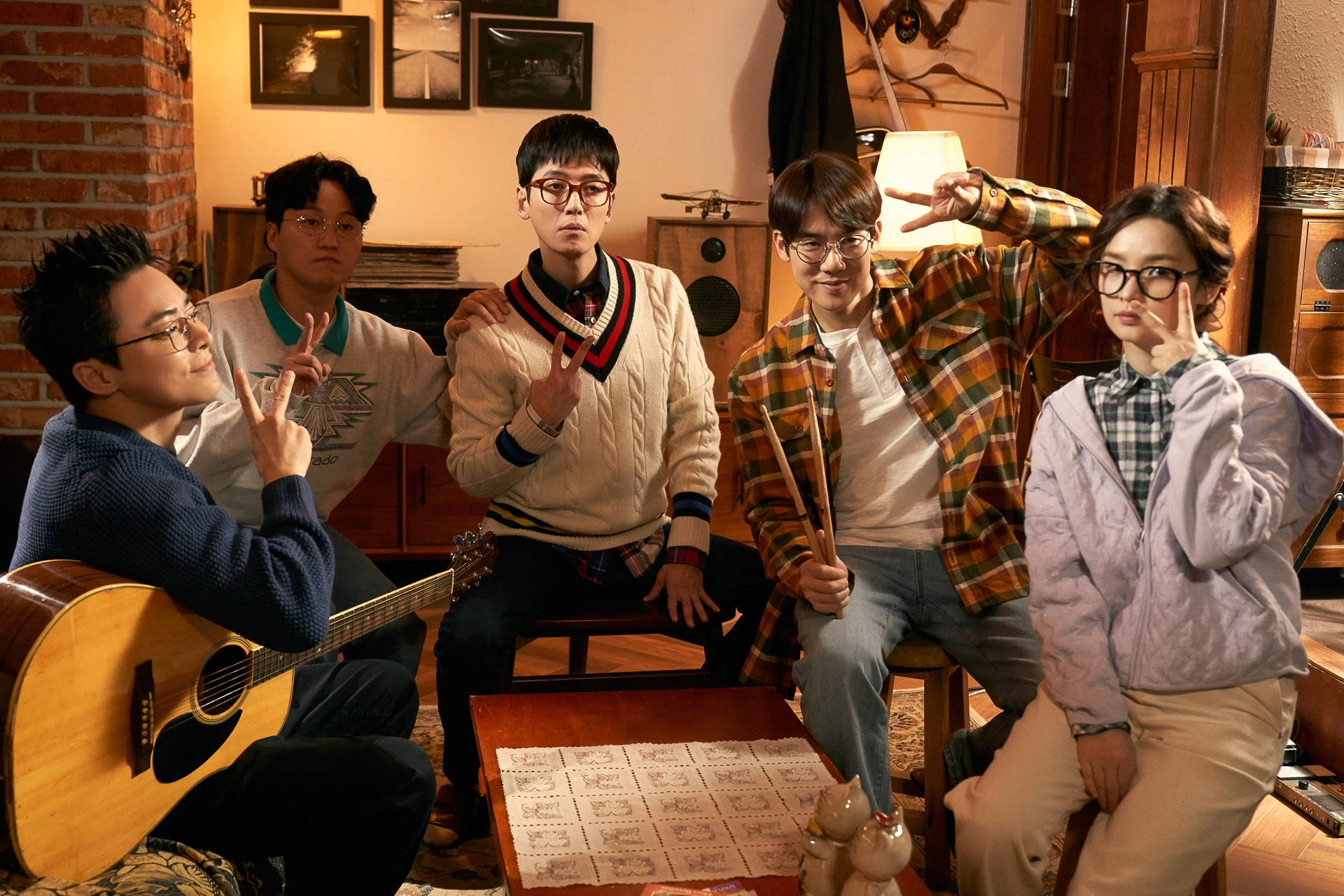 Playlist 桌布 壁紙 — 五位年輕音樂家在一個舒適的磚牆房間裡，拿著樂器並做出俏皮的手勢。
