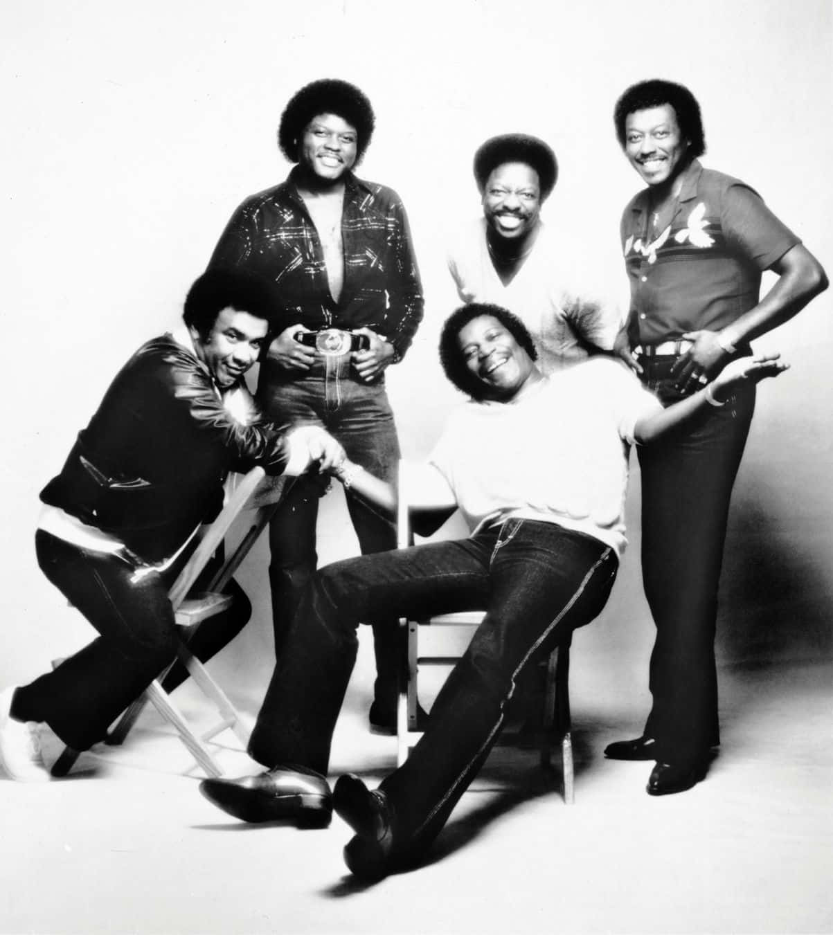 Rappers 桌布 壁紙 — 五位微笑男士身穿1970年代時尚，在簡約的攝影棚背景前與椅子擺出俏皮姿勢。